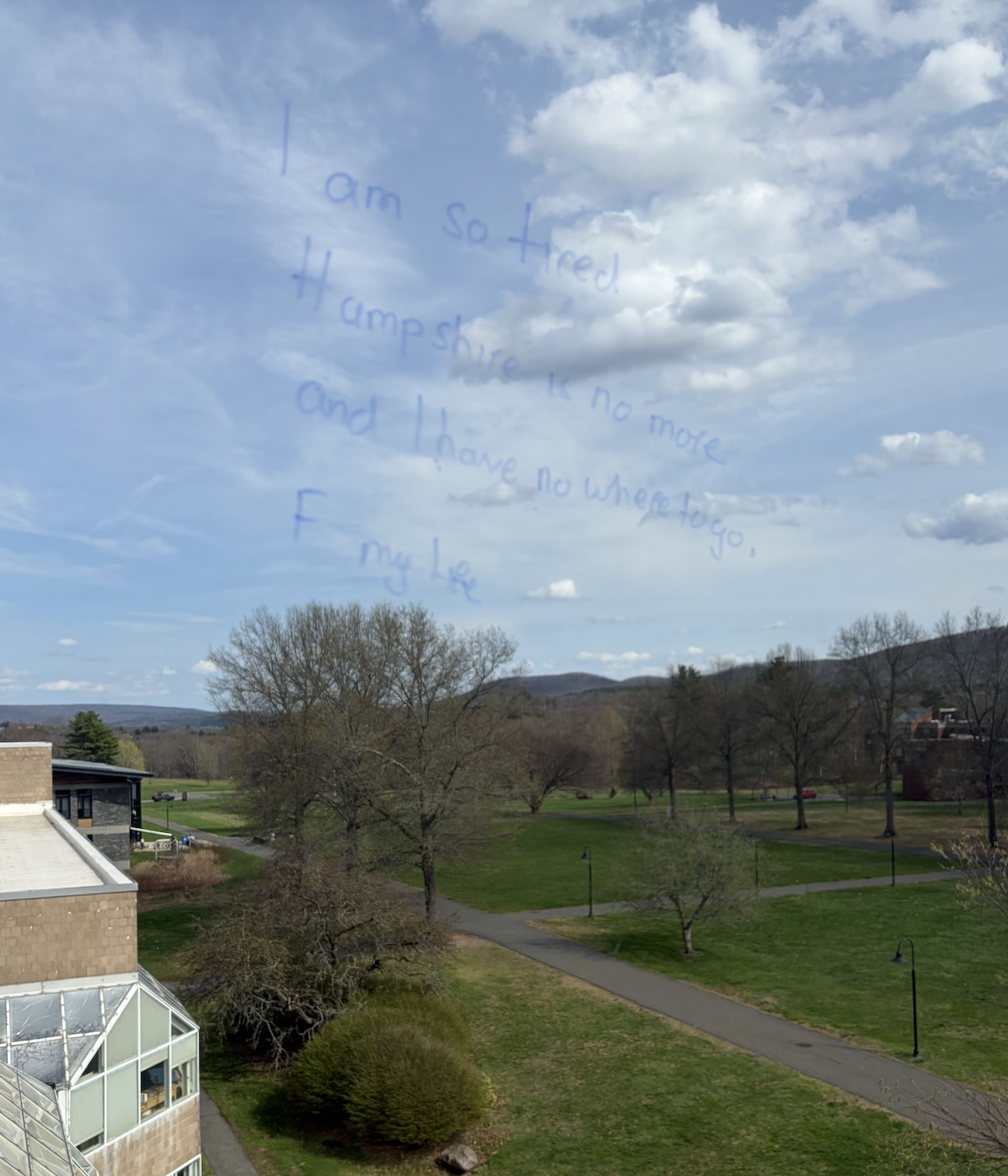 Clouds and blue sky visible through a window with a handwritten note written on the glass that says, 'I am so tired. Hampshire is no more and I have no where to go, F my life.'