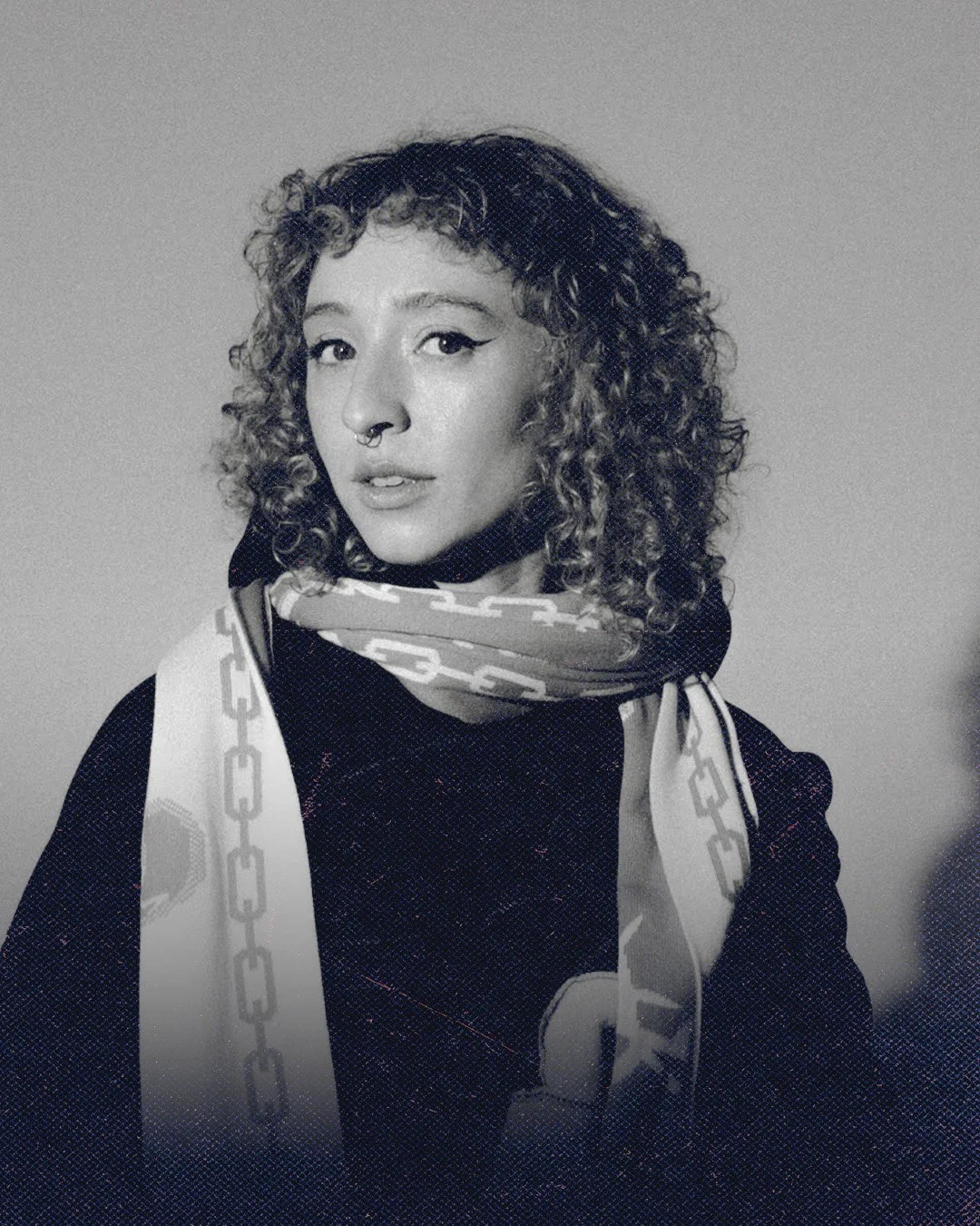 Black and white portrait of a woman with curly hair, wearing a scarf and a jacket, looking at the camera.
