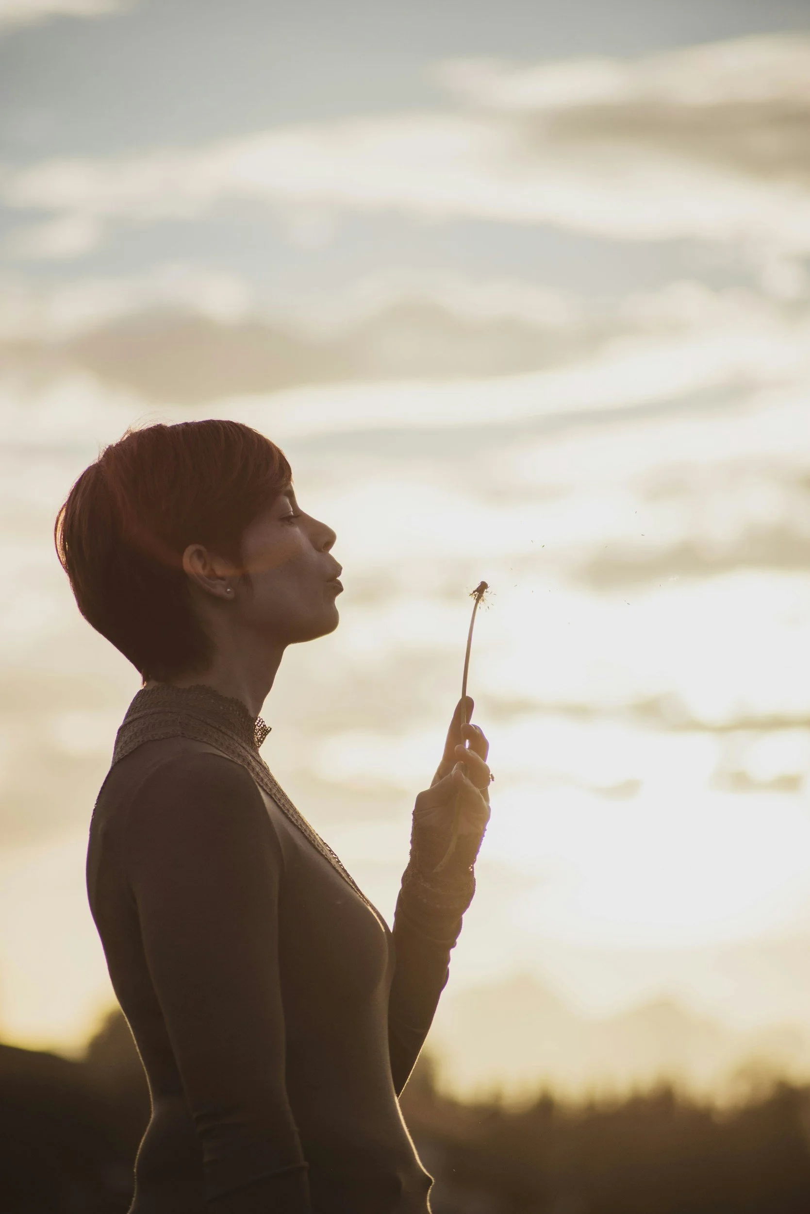 Side profile of a mom outside blowing on a dandelion that she is holding