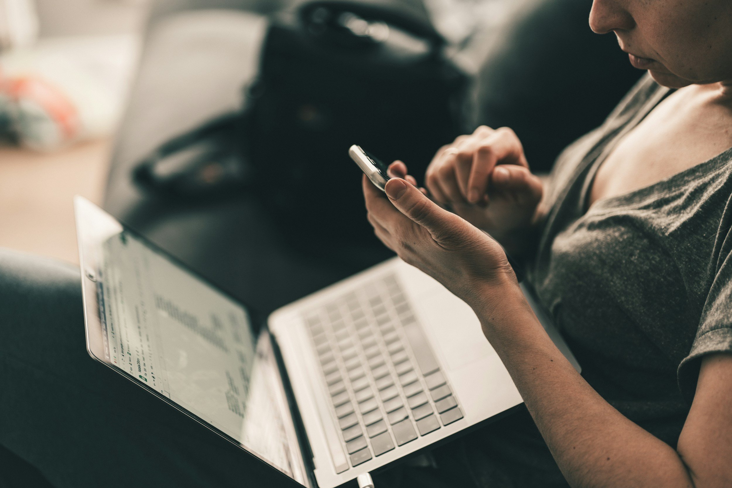 woman looking down at her phone with a laptop computer on her lap