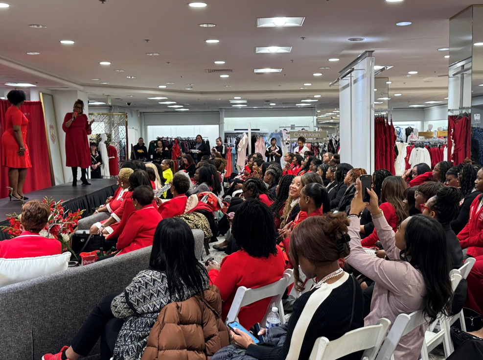 Women dressed in red attending a speech at a women's event inside a retail store.