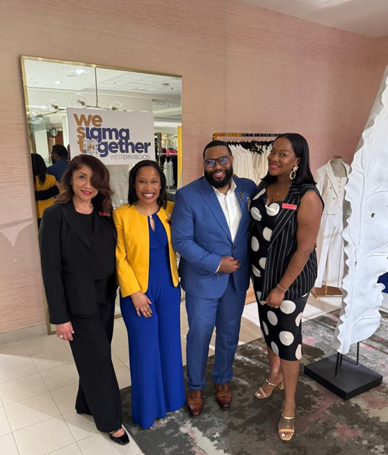 Four people standing in front of a "We Sigma Together" sign at a retail store, smiling for the photo.