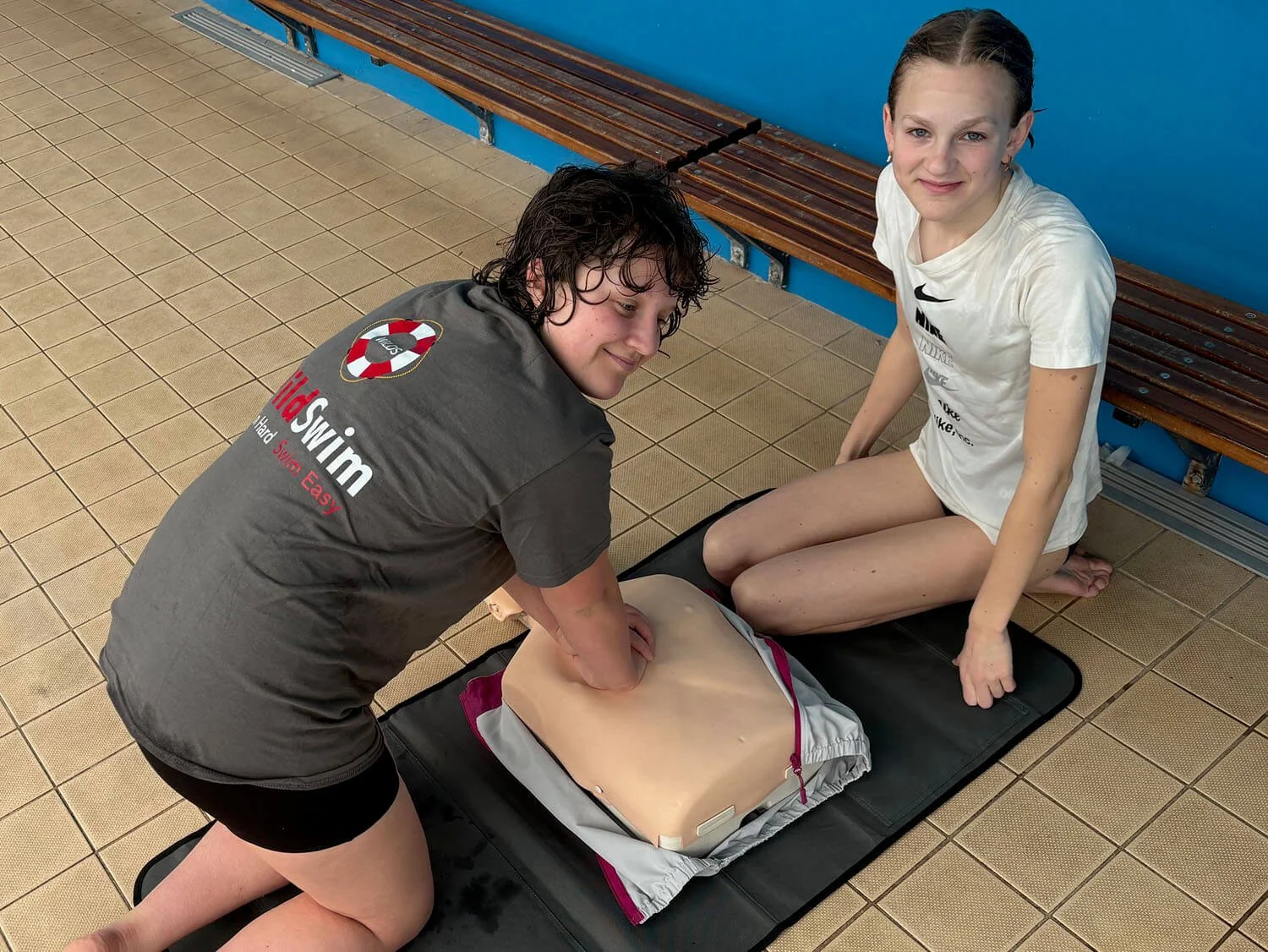 Two young women sitting on the ground practicing CPR training on a training dummy