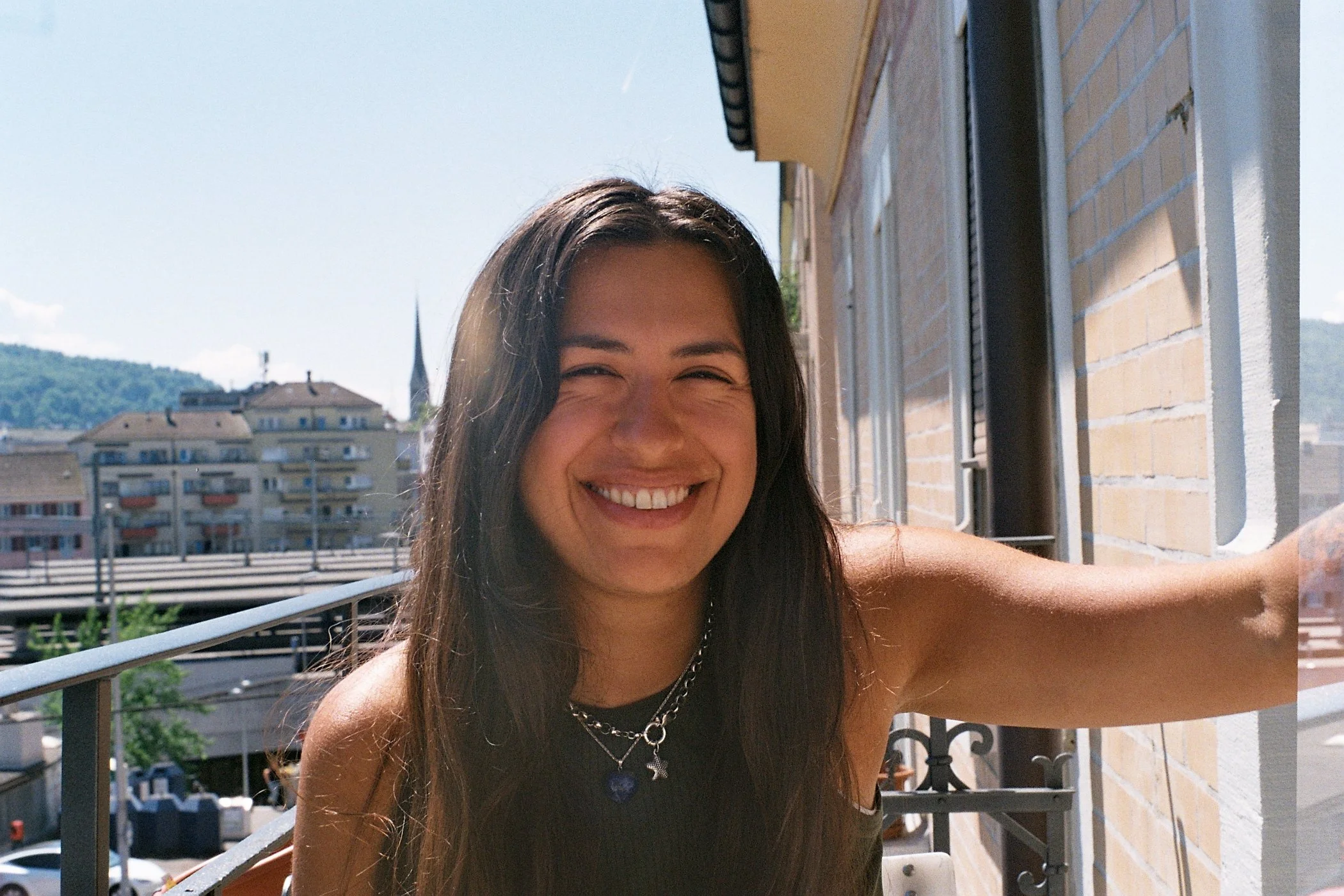 Junge Frau, die auf einem Balkon in einer Stadt bei sonnigem Wetter lacht.