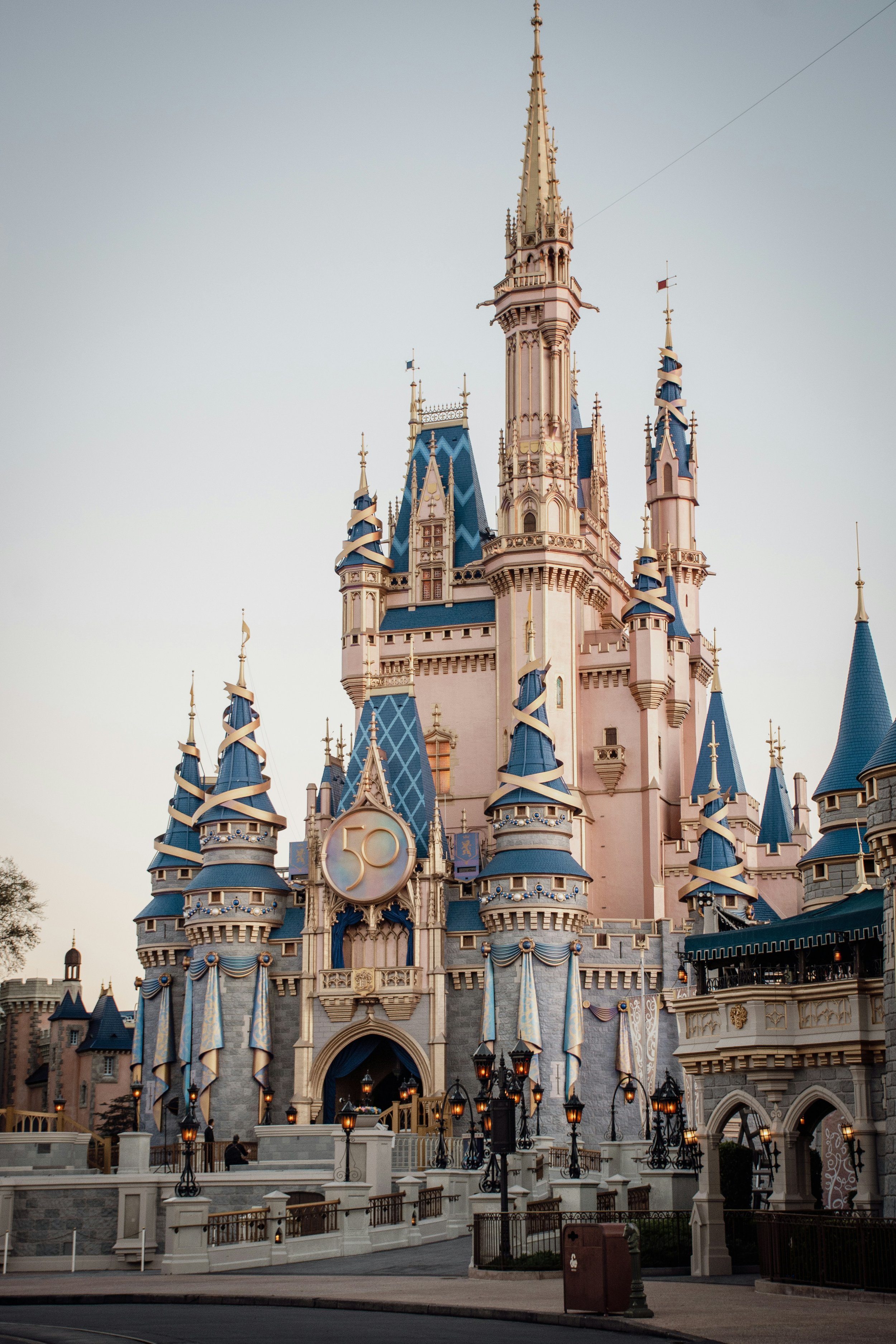 Disney's Sleeping Beauty Castle decorated for its 50th anniversary at Disneyland, with blue and pink turrets and celebratory banners.