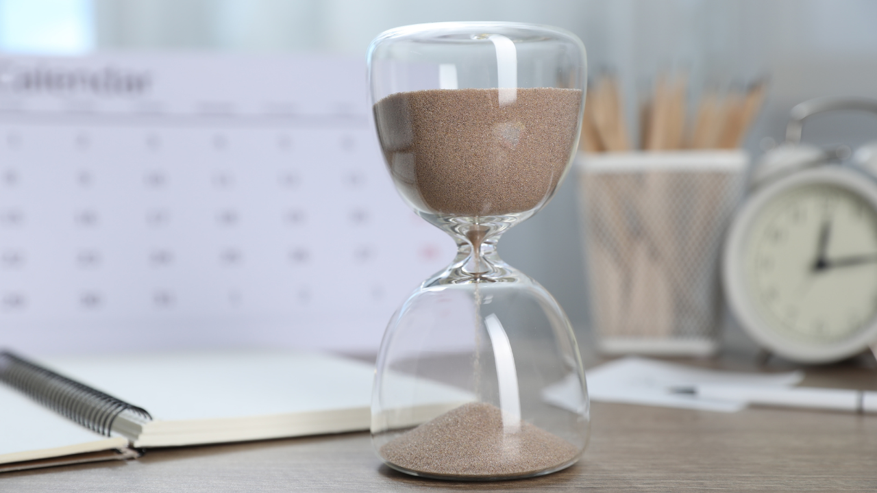 Deadline. Hourglass with Flowing Sand, Stationery, Calendar and Alarm Clock on Wooden Table Indoors