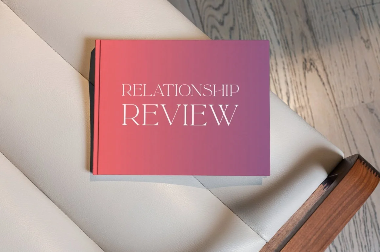 A pink and purple gradient book titled 'Relationship Review' resting on a white leather chair with a wooden armrest.