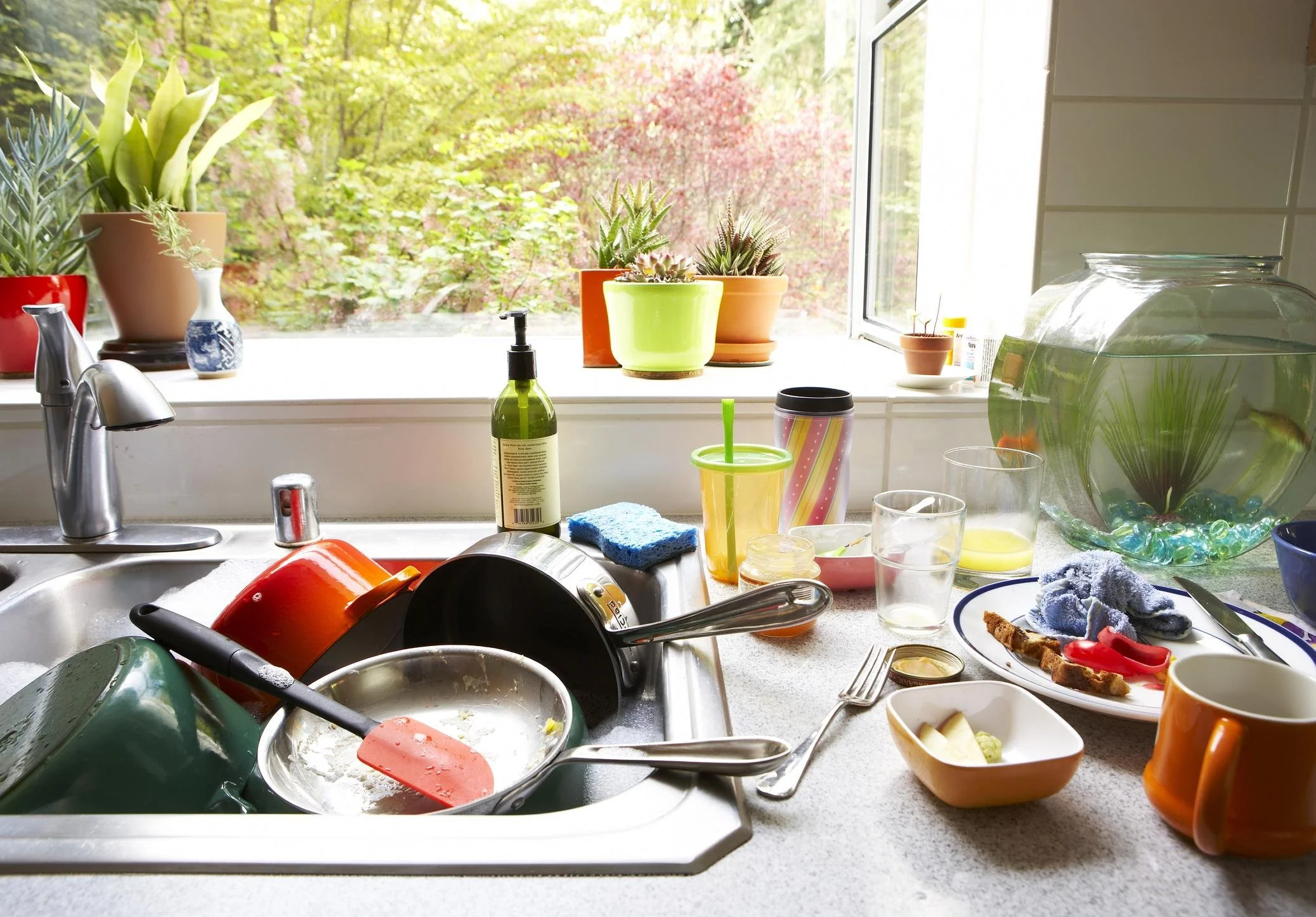 Sunlit kitchen with dishes piled in and around the sink.
