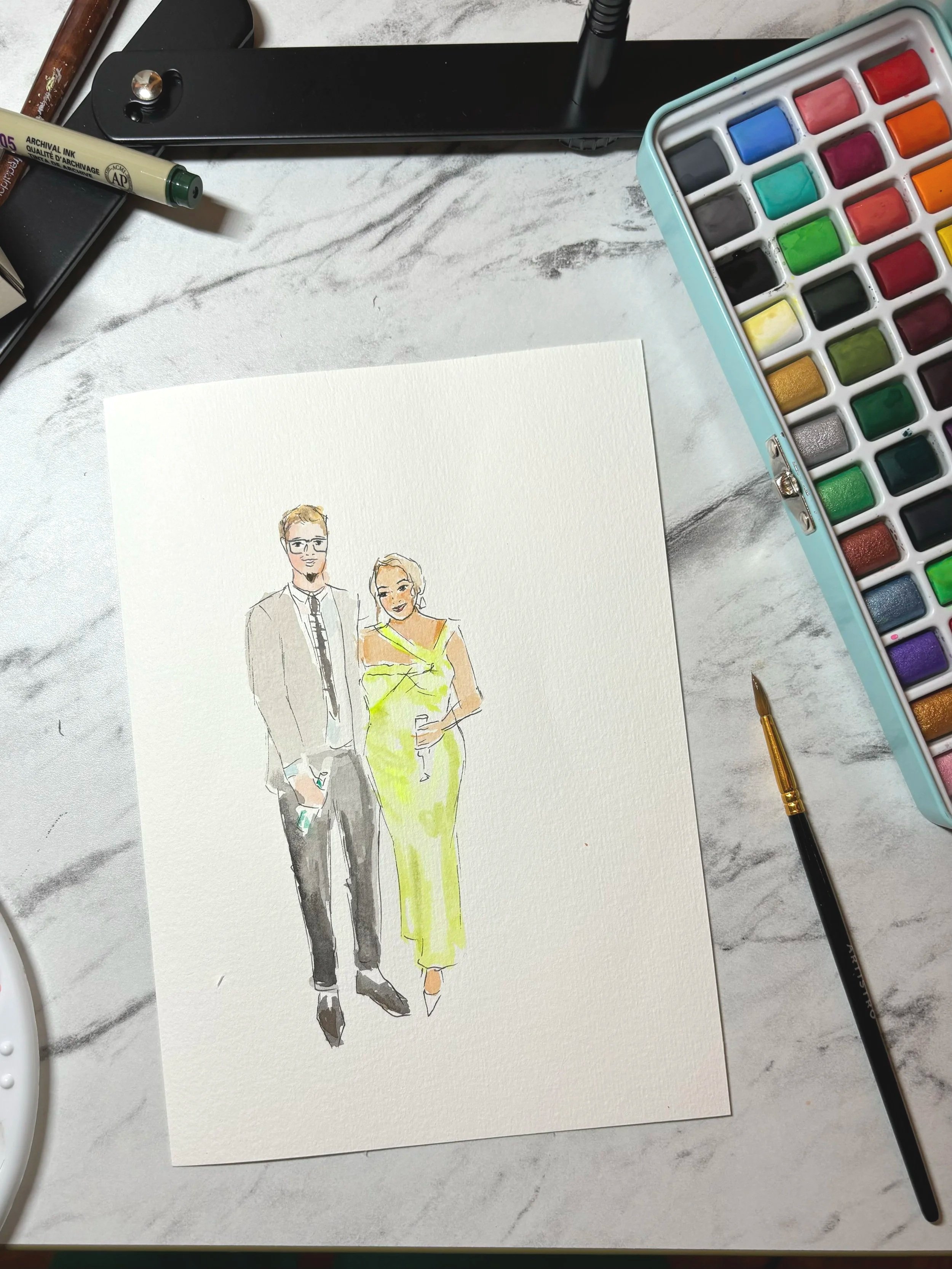 A watercolor painting of a man and woman dressed in formal attire, with the man in a gray suit and tie and the woman in a yellow dress, placed on a white marble surface surrounded by art supplies including watercolor paints, a gold brush, and a black