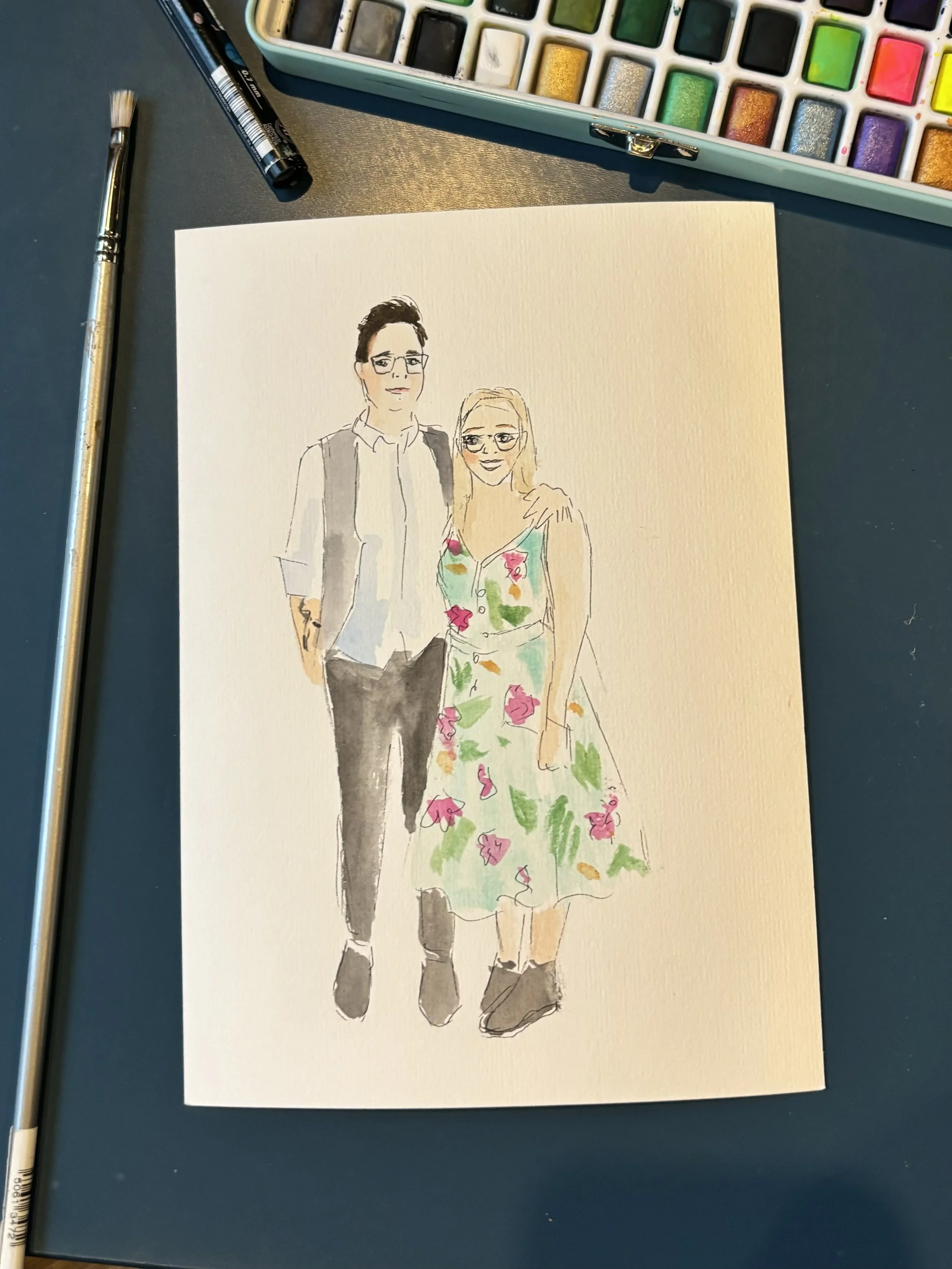 A watercolor illustration of a man and woman standing close together. The man has dark hair, glasses, and is wearing a light shirt with darker pants and a shoulder bag. The woman has blonde hair, glasses, and is wearing a floral dress. They are smili