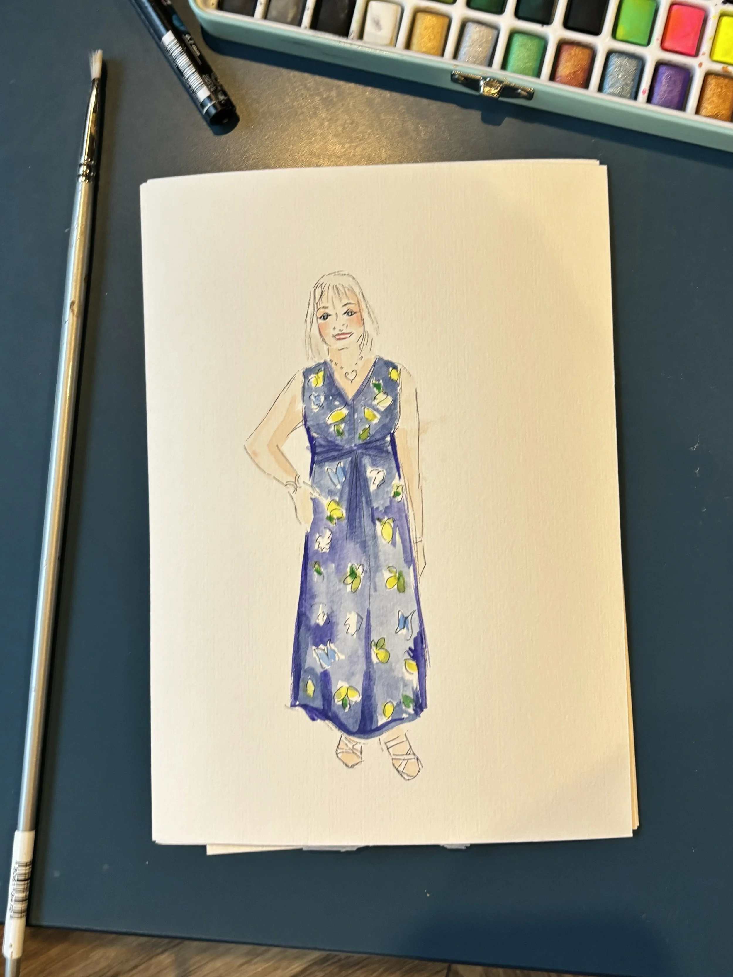 A hand-drawn sketch of a woman in a blue dress with yellow and white lemon patterns, standing with one hand on her hip and smiling.