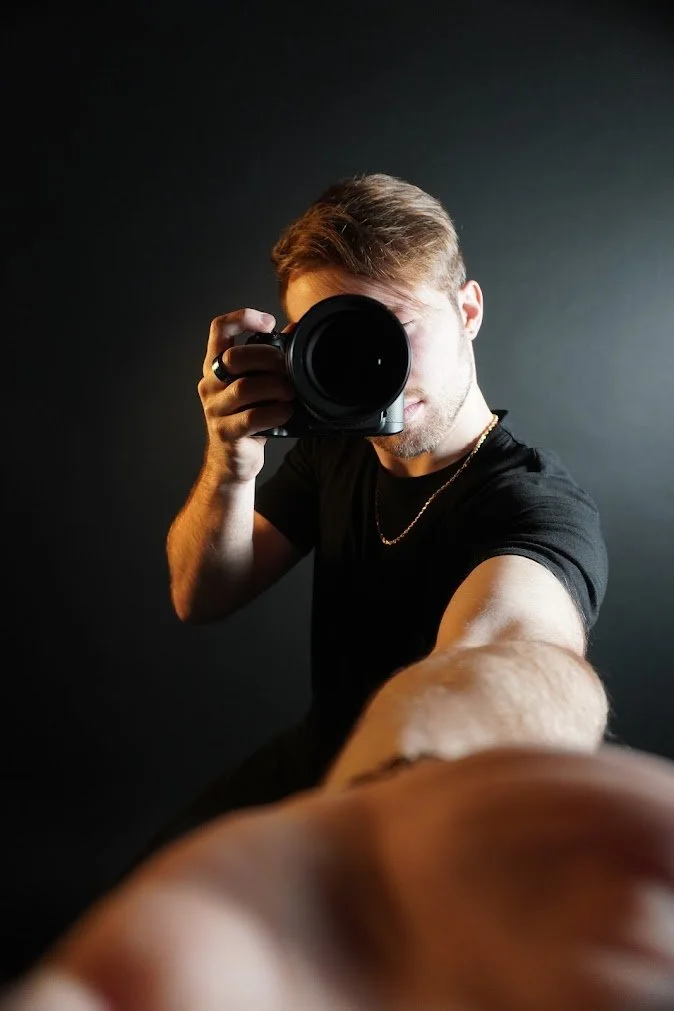 Young man taking a selfie with a professional camera against a dark background