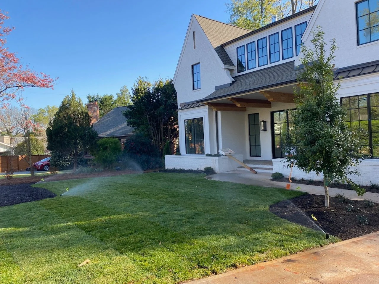 Newly landscaped front yard with fresh sod, sprinkler irrigation, and young trees at a North Carolina home