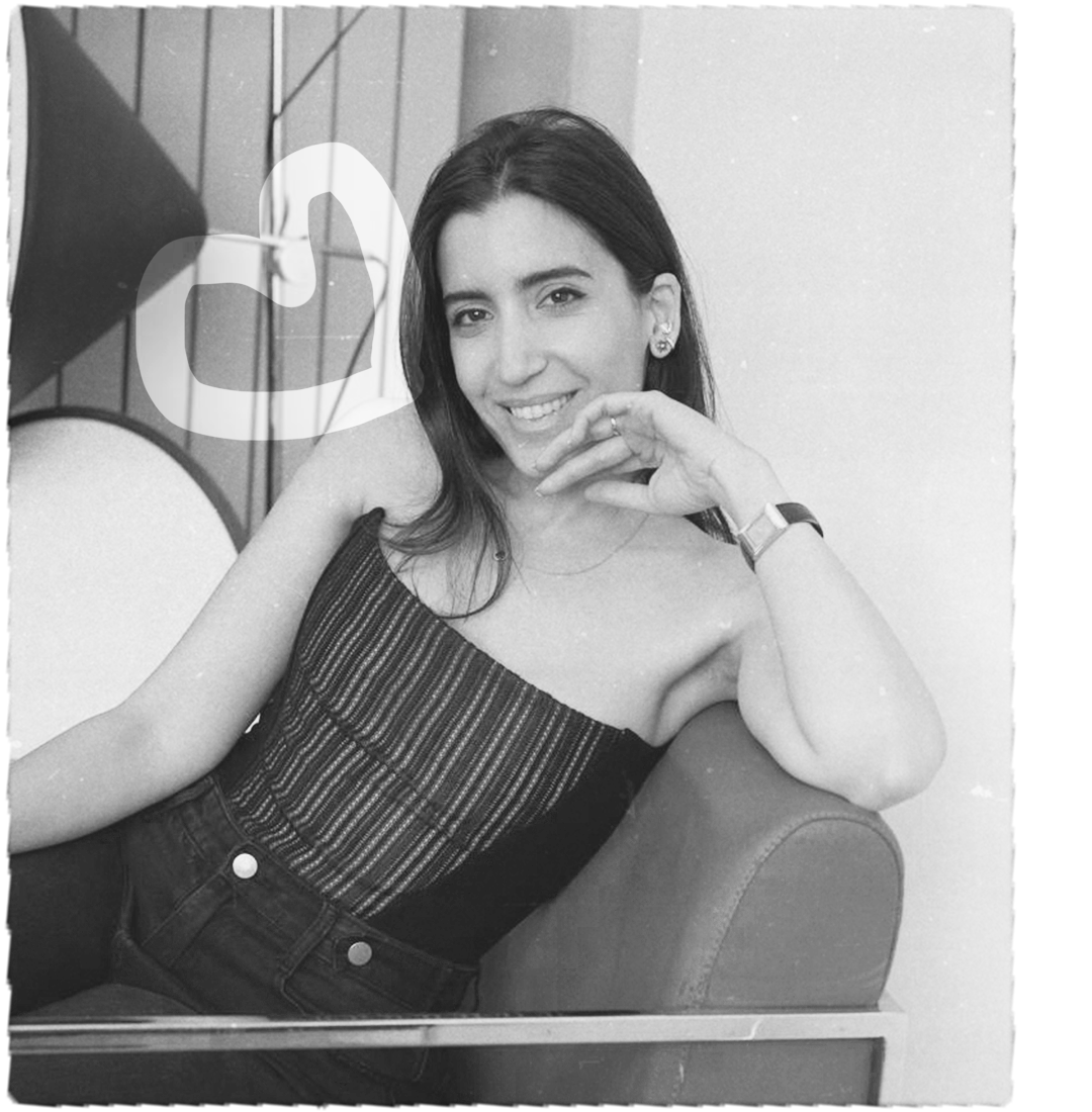 A woman with dark hair smiling and resting her head on her hand, sitting on a couch with a wall and some decorative elements in the background. Beef Design Studio, Brand strategy, Brand identity, visual identity, graphic design, testimonial.