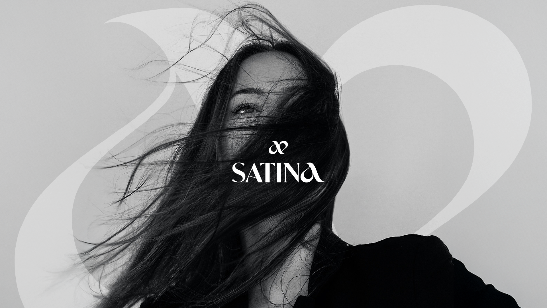 Black and white promotional image of a woman with long hair blowing across her face, featuring the brand name 'SATINA' in the center. Promotional image for satina, a brand strategy and visual identity project to help bring their brand to life