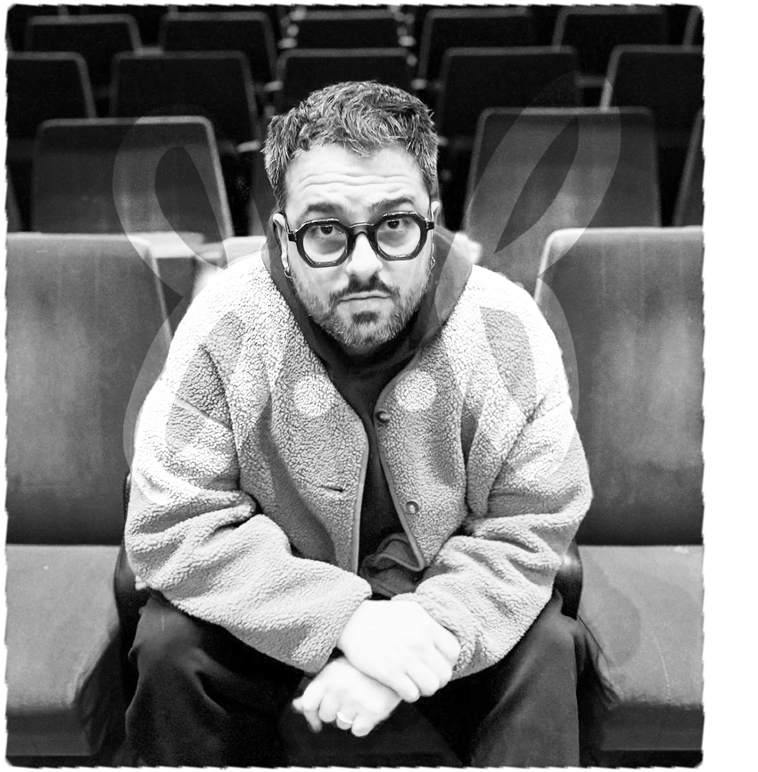 A man with glasses and a beard sitting on a chair in an auditorium or theater, with empty chairs behind him. Beef Design Studio, Brand strategy, Brand identity, visual identity, graphic design, testimonial.