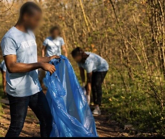 People participating in a trail cleanup, collecting trash in a wooded area during autumn.