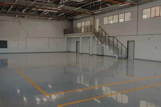 Empty indoor sports or warehouse space with polished concrete floor, marked with yellow boundary lines, and staircase leading to an office or mezzanine level.
