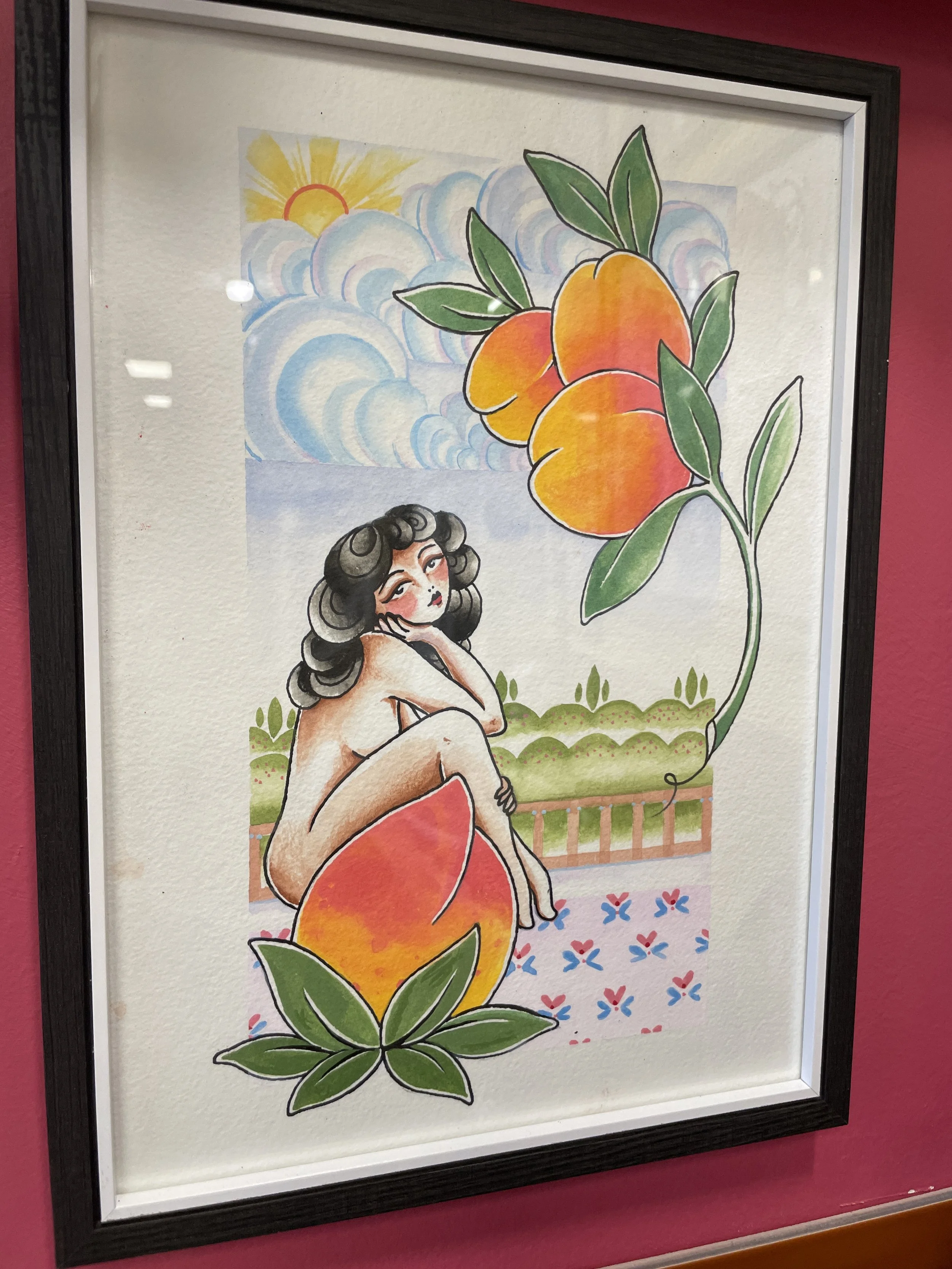 A framed watercolor painting showing a woman with dark curly hair, sitting and touching her face. Behind her are three large peaches with green leaves, and in the background, there's a sky with stylized clouds and a yellow sun with rays.