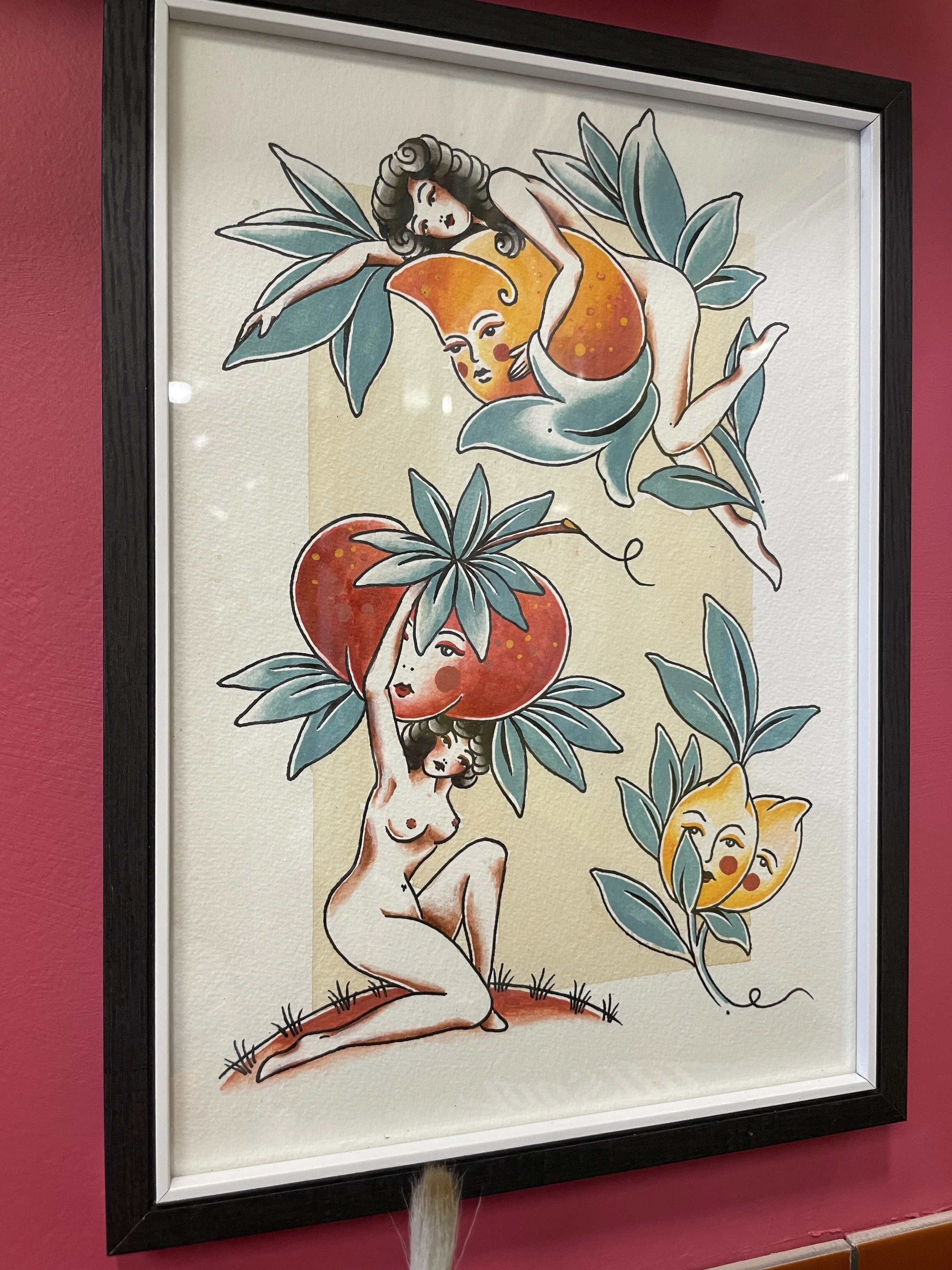 A framed illustration featuring a reclining nude woman with curly hair cradling a peach and another holding a tomatoes with a face , lemons with faces  characters with red cheeks.
