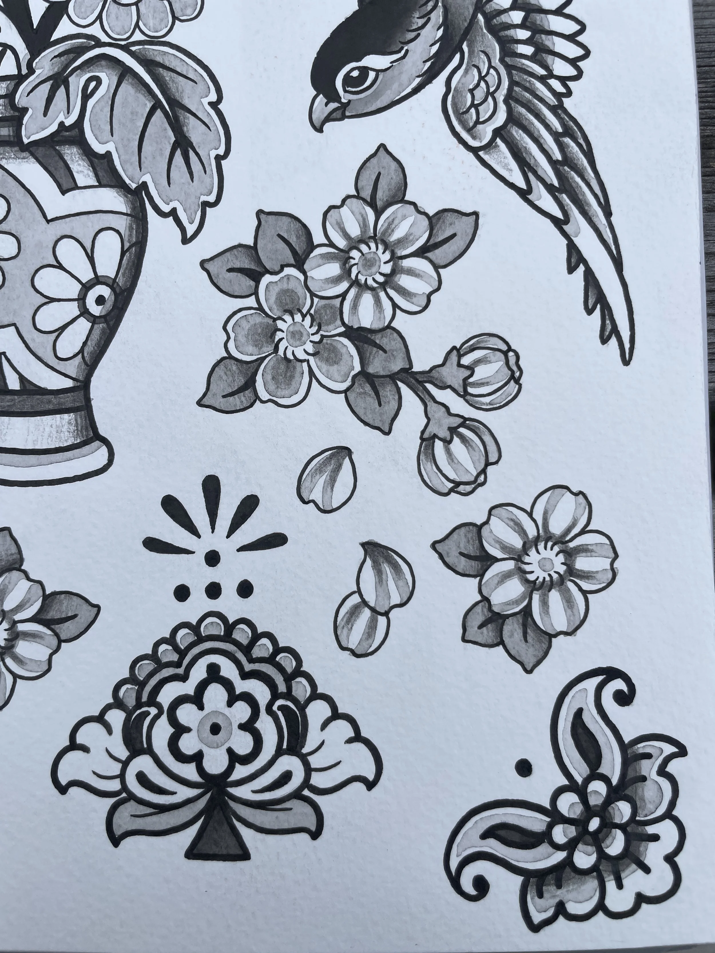 Black and white line drawing of flowers, leaves, a bird, a vase, and decorative patterns on paper.