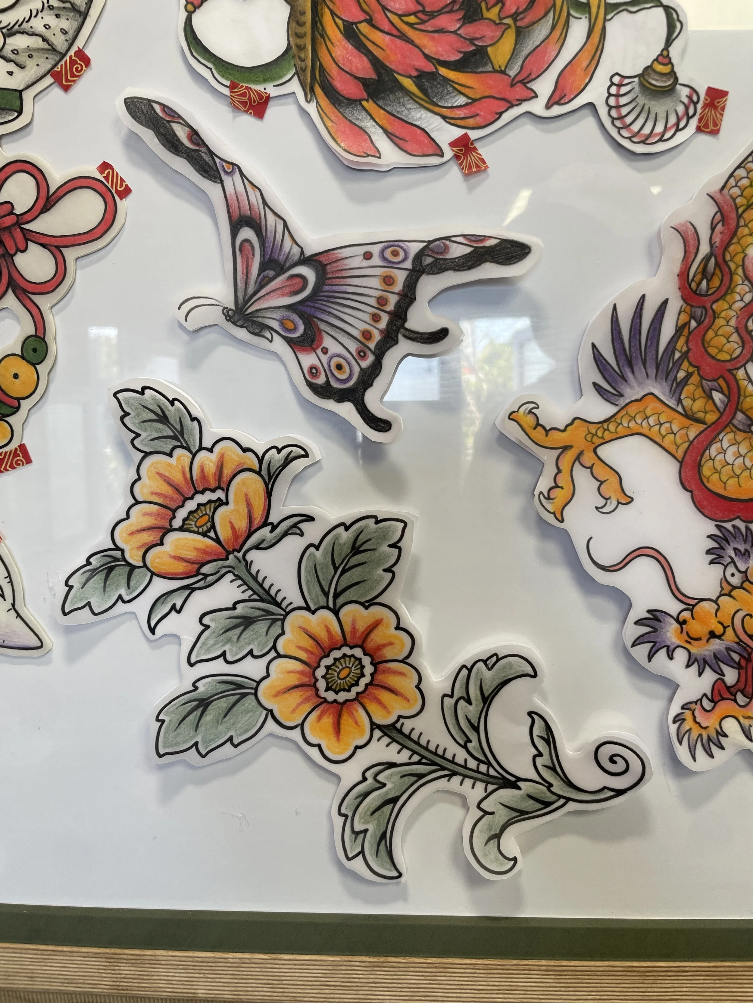 Colorful paper cutouts of flowers, butterfly, and other designs typical of traditional Asian art, placed on a white surface.