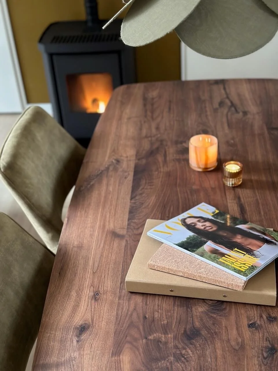Een houten eettafel met een tijdschrift, een klapper en twee kaarsen, met een haard in de achtergrond.