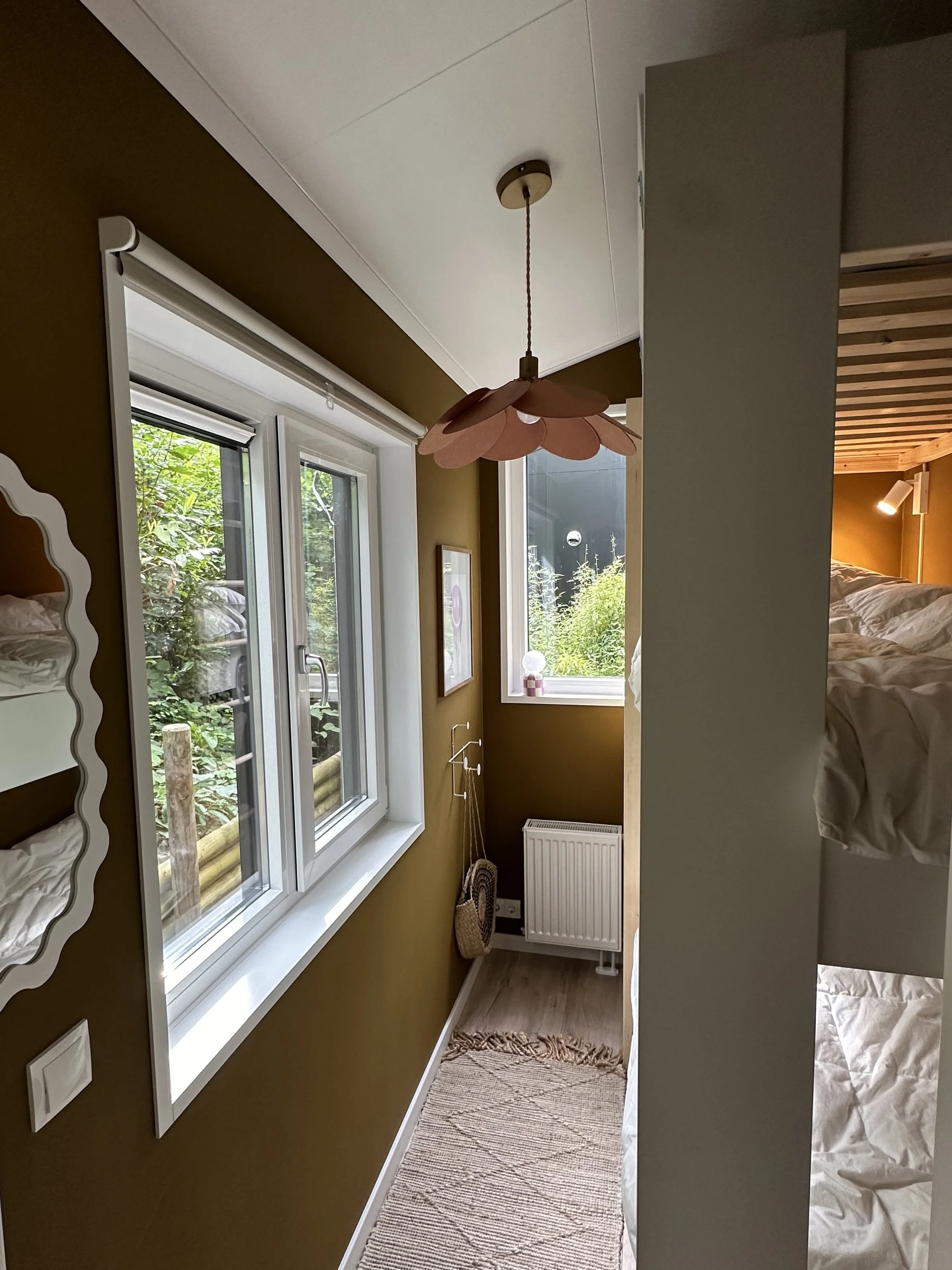 Binnenzicht van een slaapkamer met een bed, een kast, een raam, een radiator, een lampenvoet met een bloemenpatroon en een tapijt.