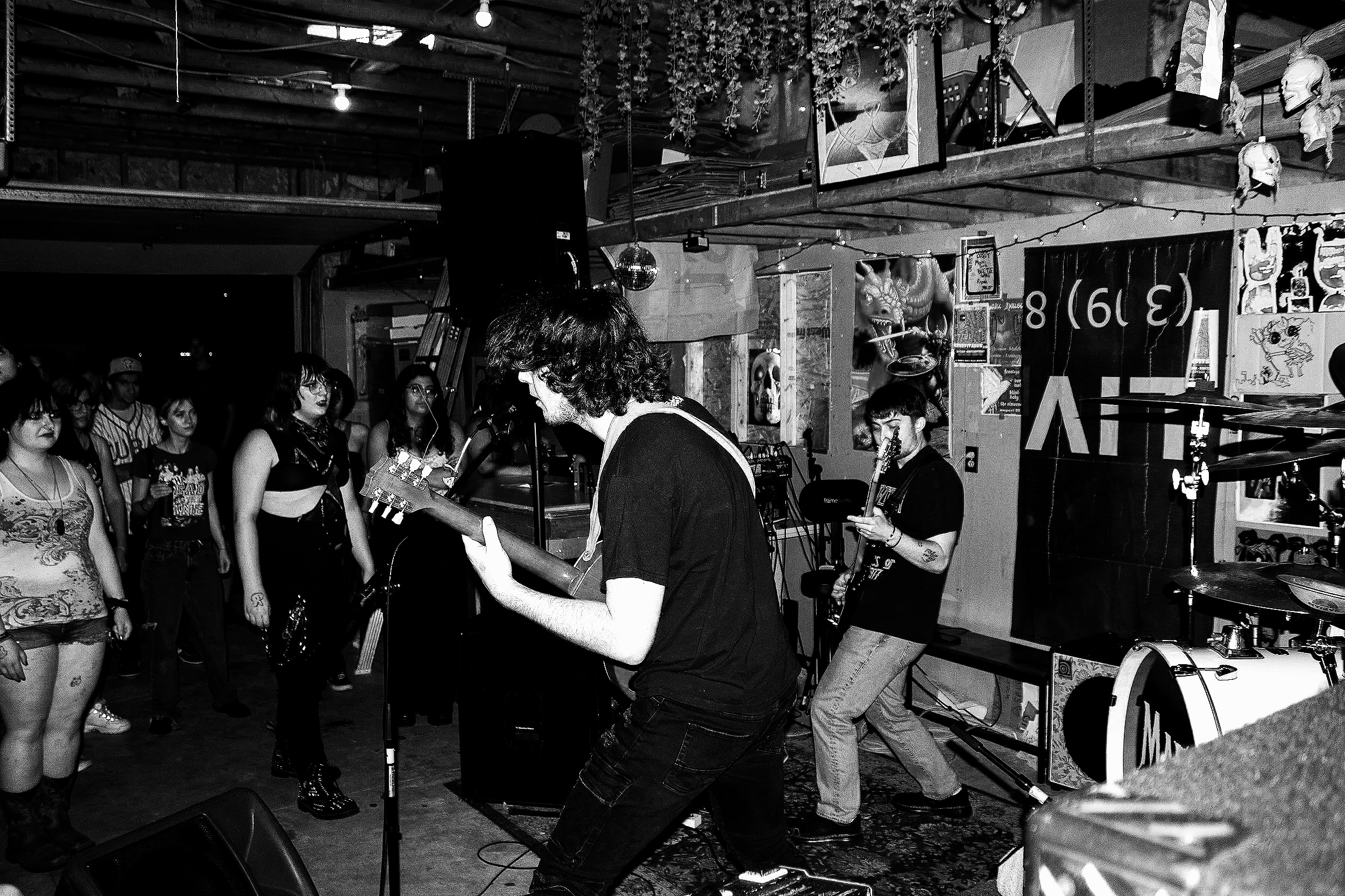 A music performance with a group of people, some playing guitars and others singing, in a rustic indoor setting with decorated walls and ceiling.