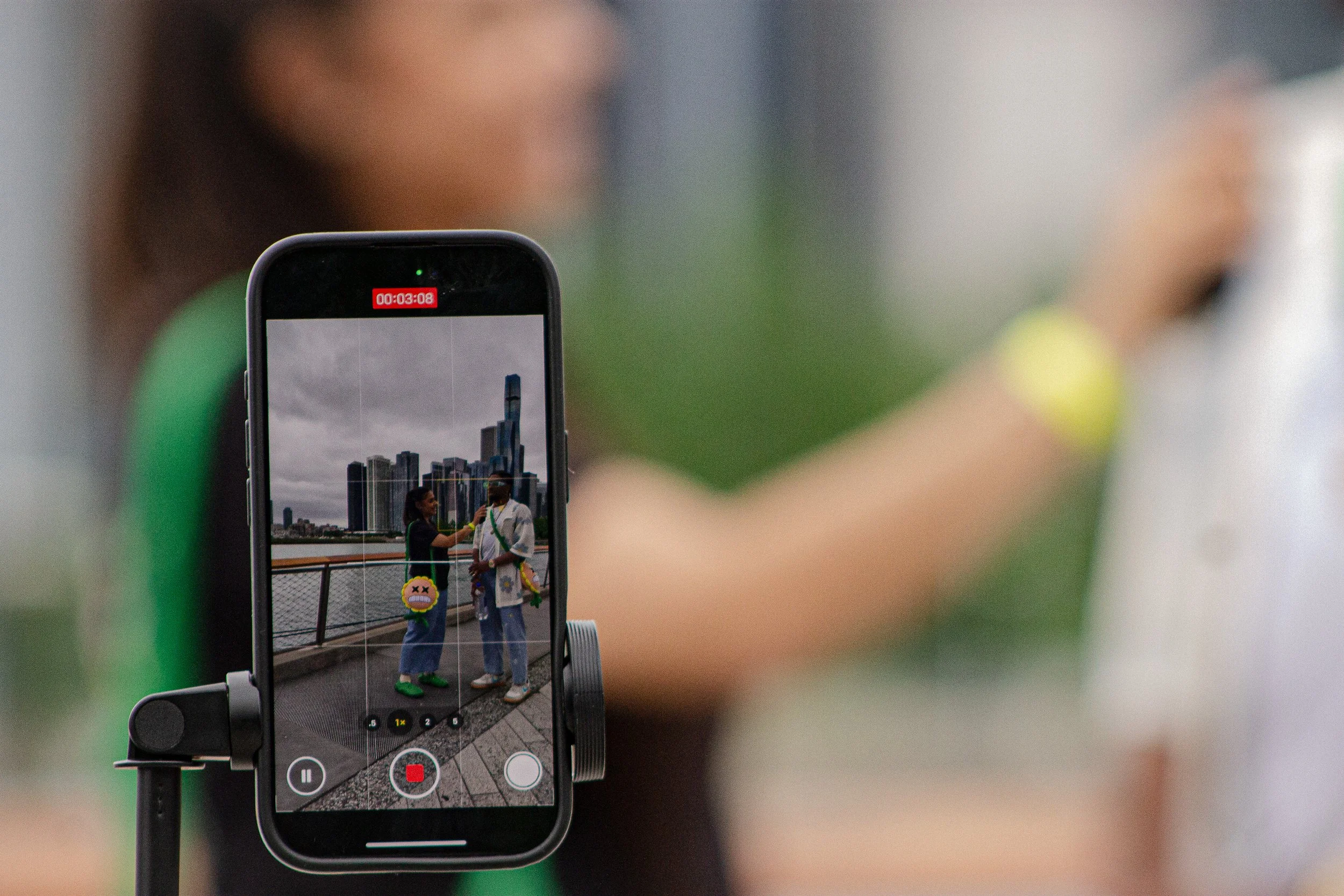 A smartphone on a tripod capturing a photo of two people standing outdoors with a city skyline in the background.