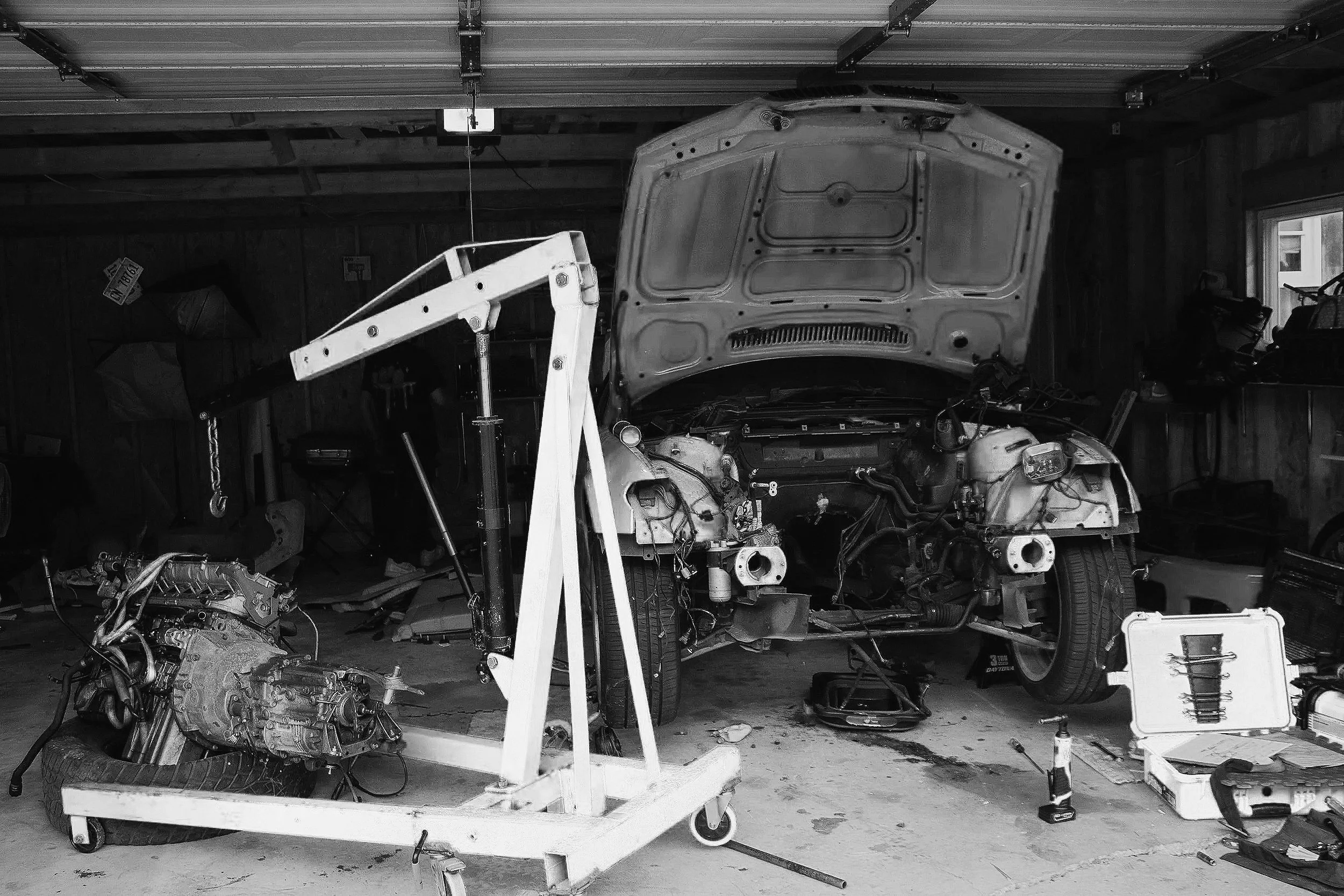 A garage workshop with a disassembled car on a lift, surrounded by various car parts, tools, and equipment.