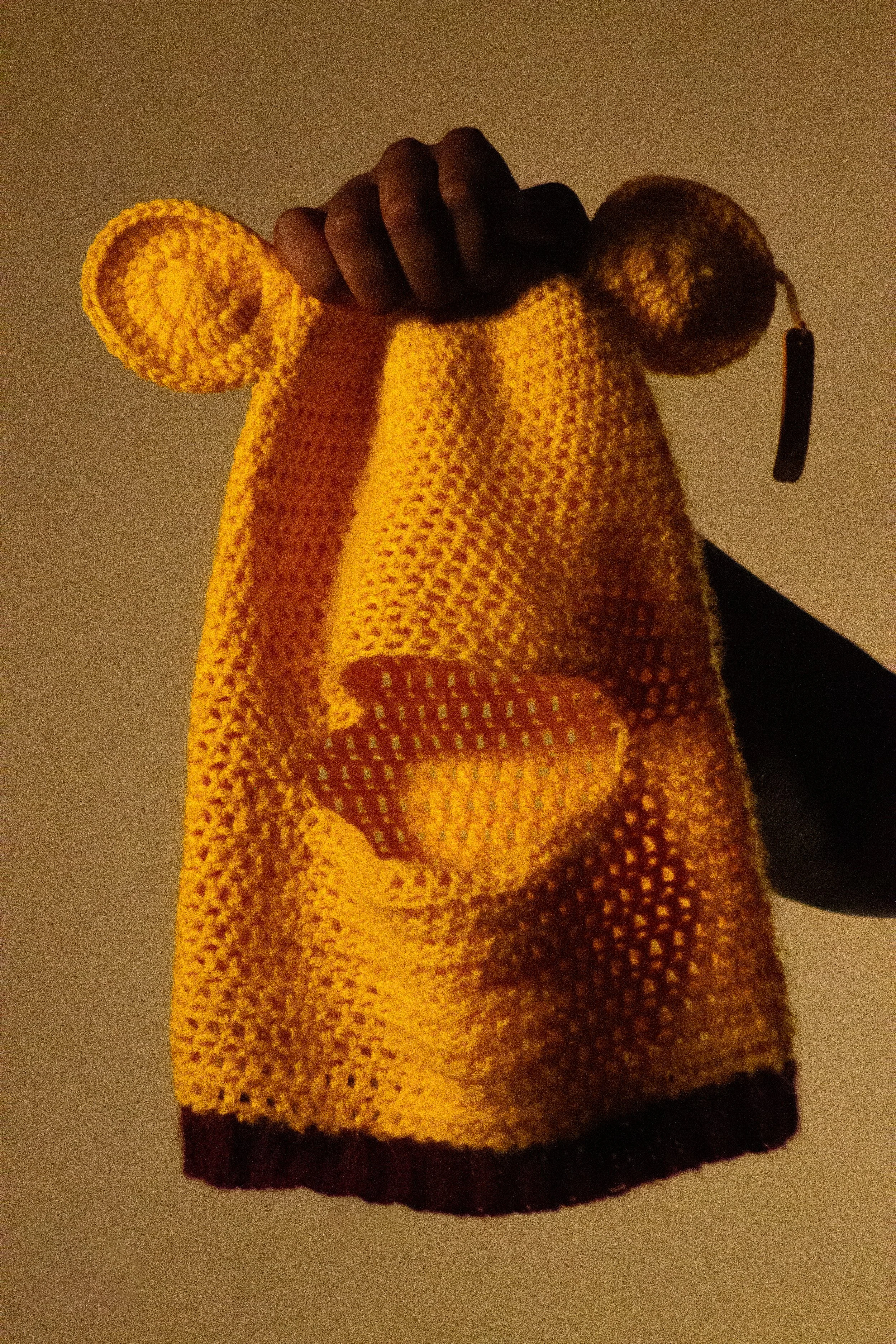 A person's hand holding a yellow knitted sock with dark brown accents at the toe, heel, and cuff.