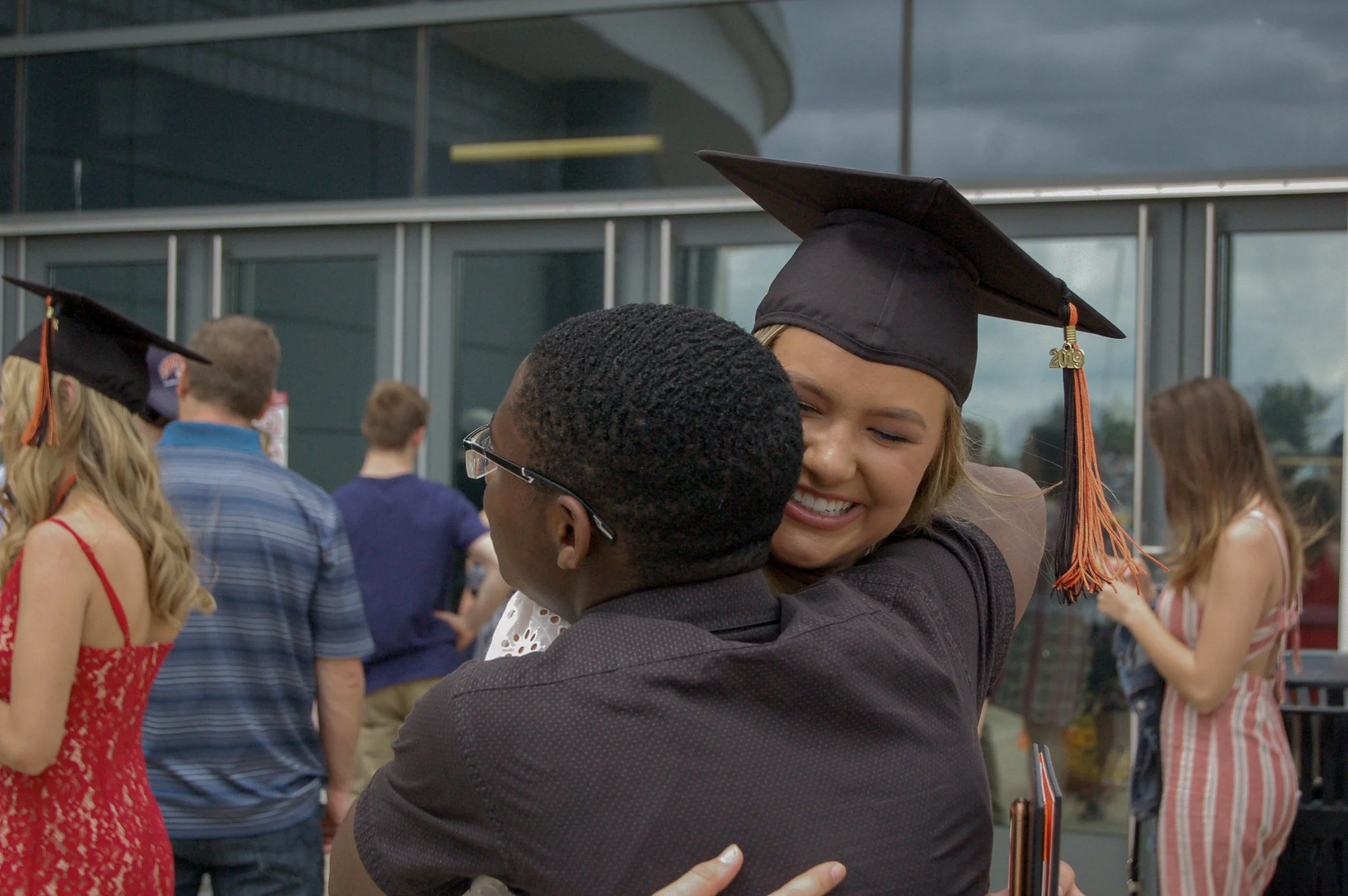 A young woman in a graduation cap hugging a person outdoors during a graduation celebration.