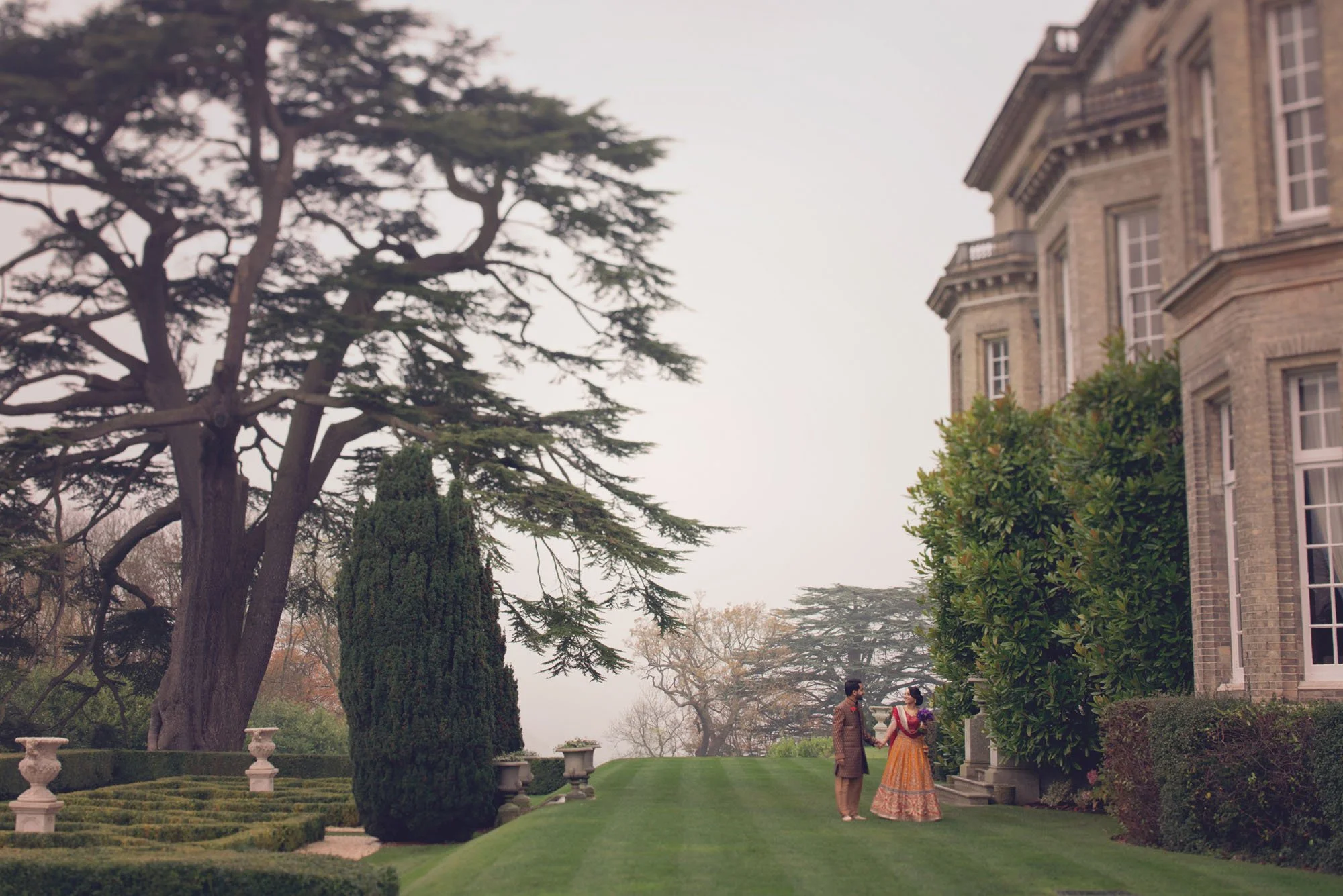 An asian bride and groom walk hand in hand in the garden during their weekday wedding at Hedsor House in Windsor 