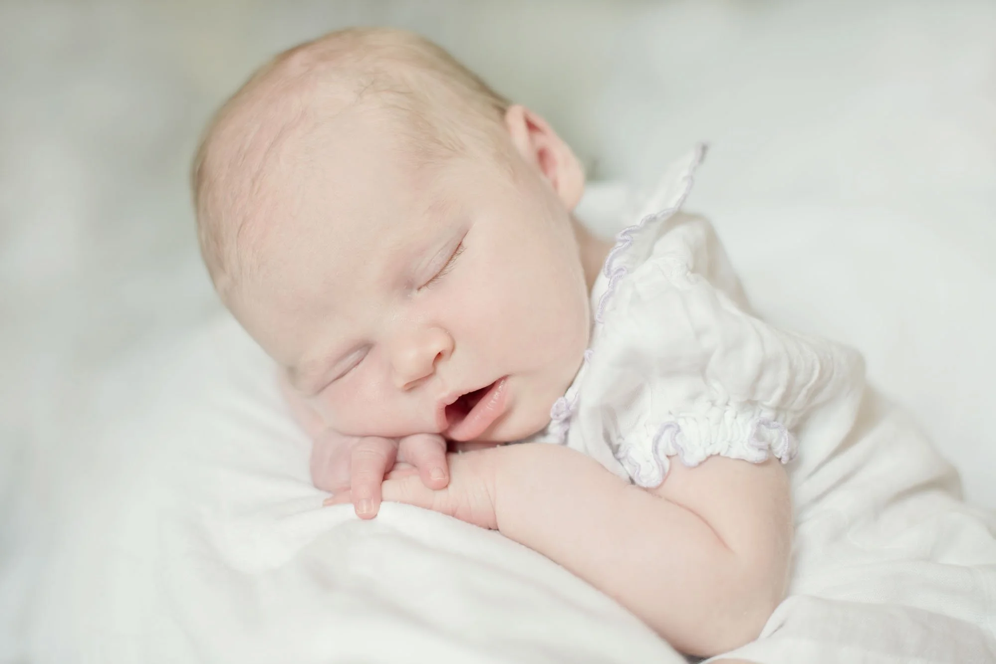 A newborn baby sleeps during a newborn photoshoot in Camden in North London. Her head is propped up on her hands and her mouth is slightly open as she sleeps.