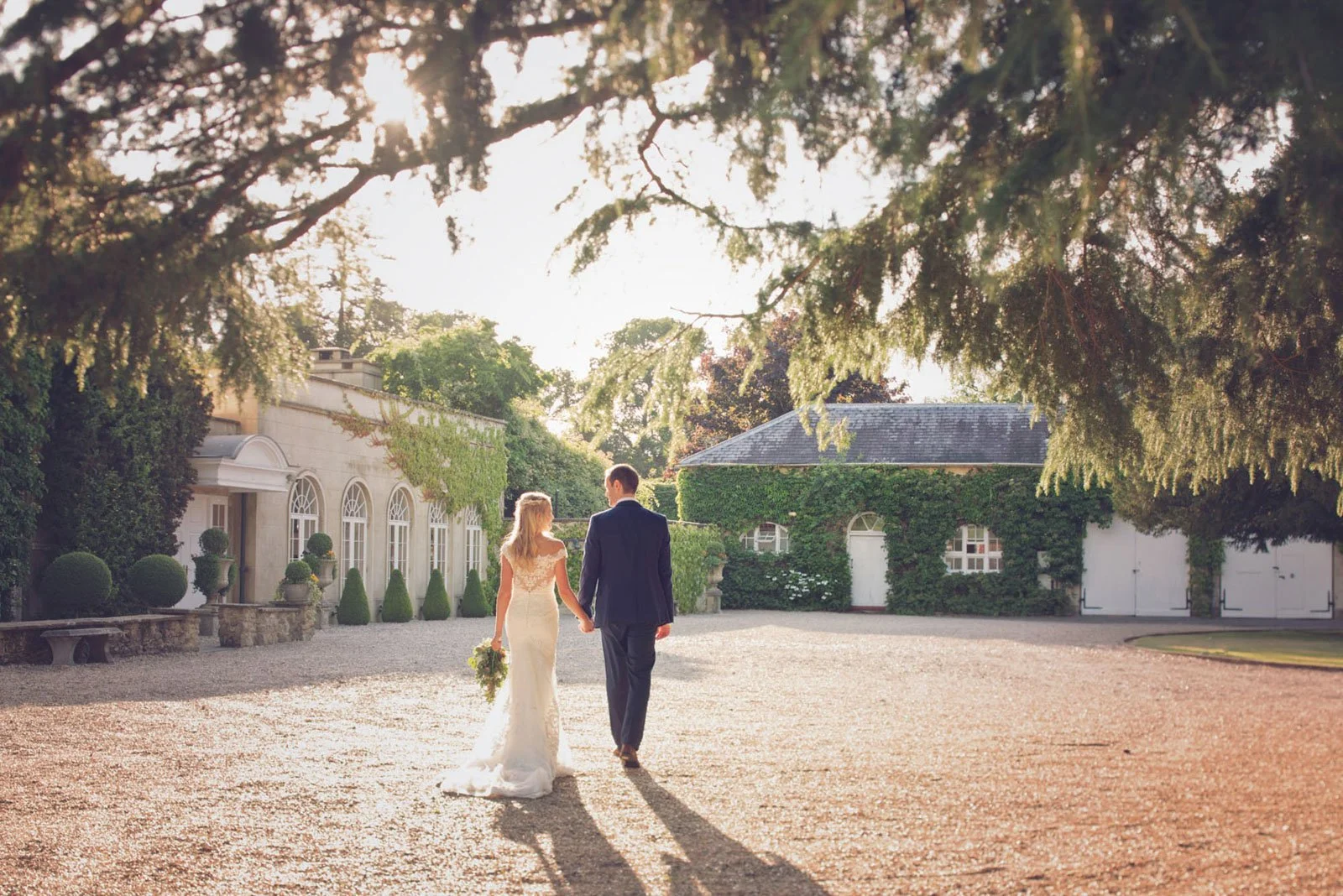 A bride and groom walk hand in hand across the courtyard at Northbrook Park in Surrey in the late afternoon sun