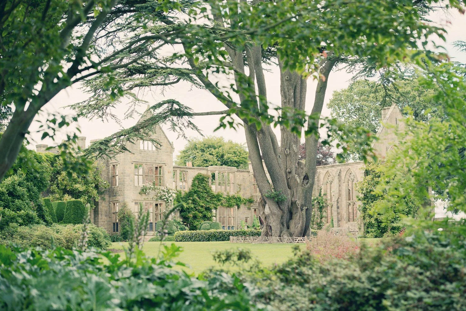A large, historic stone building surrounded by lush green trees and manicured gardens.