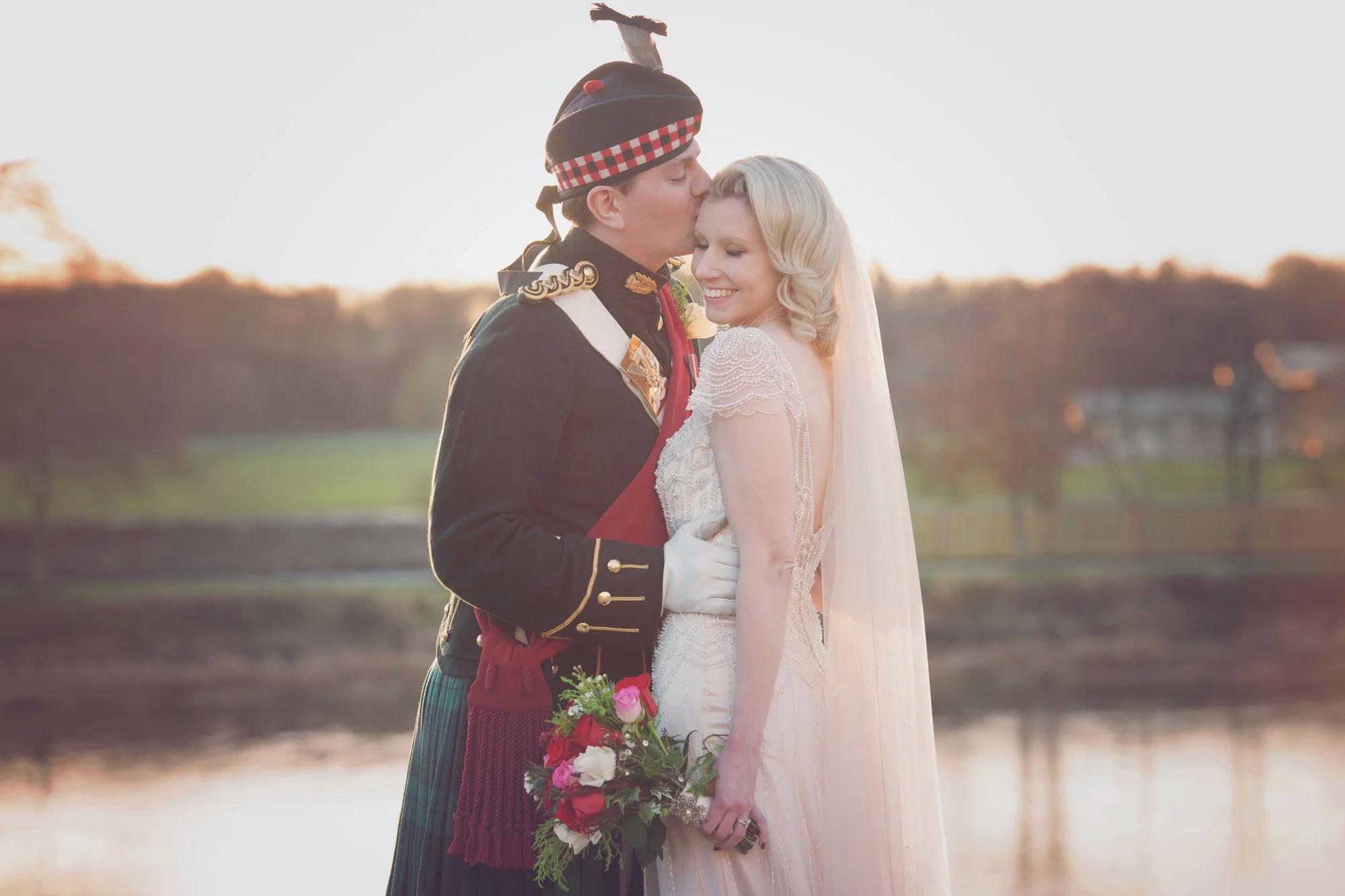 A groom, dressed in a kilt and full traditional scottish outfit, kisses his bride by the River Thames in Richmond in west London during the winter sunset.