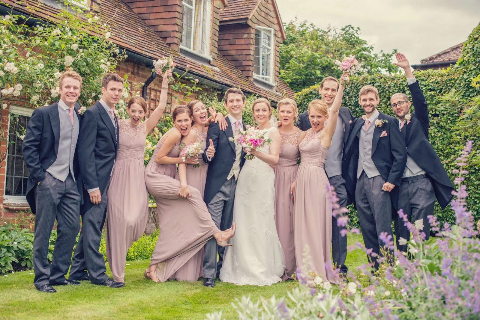 A fun-loving bridal party laughs as they have their group photo taken in the garden of the bride's parents' house in Hampstead Garden Suburbs in north London