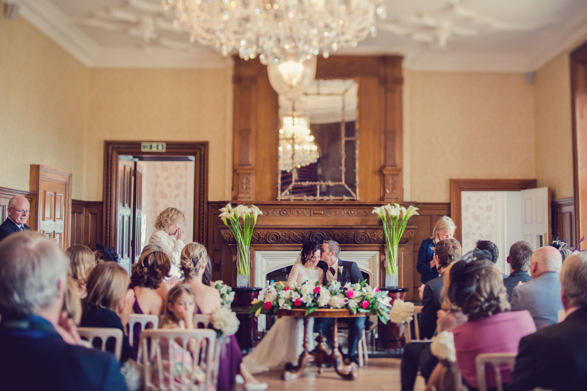 A groom whispers in his bride's ear as they sign the wedding register at Froyle Park in Hampshire