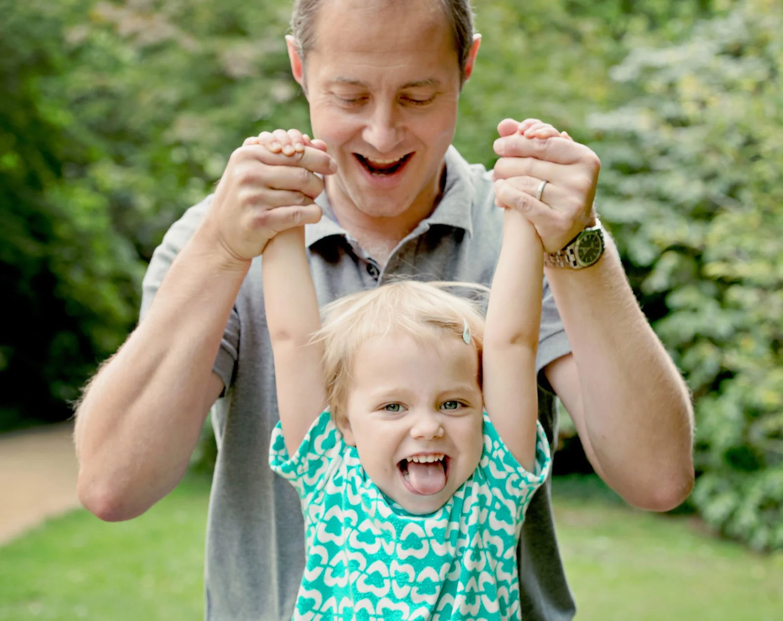 A little girl laughs and sticks her tongue out as she's swung up by her smiling father during a family photoshoot in Cannizaro Park in Wimbledon in south west London