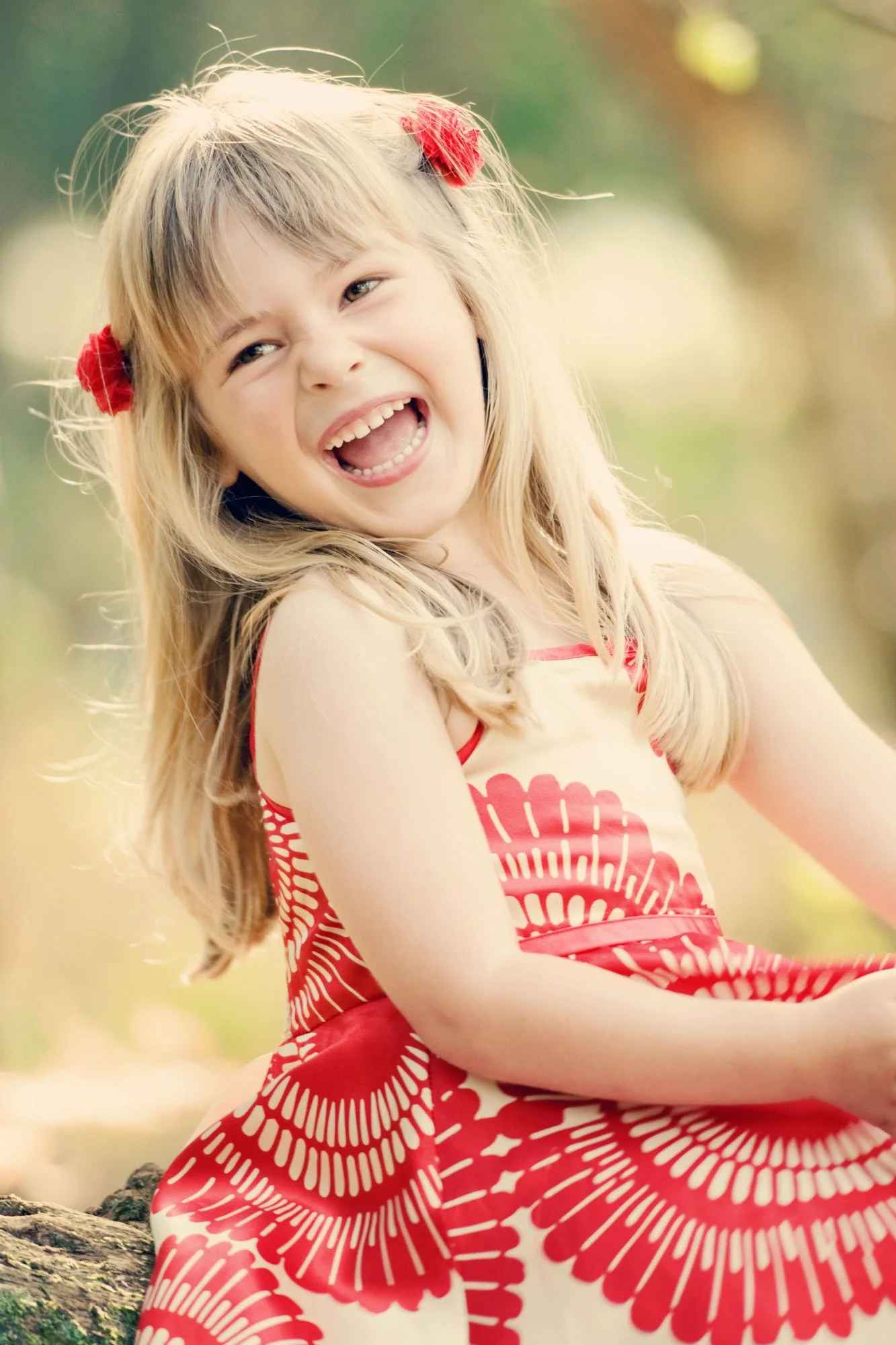 Little girl in a red and white dress laughs over her shoulder in the late afternoon sun during a family photoshoot in Hyde Park in London