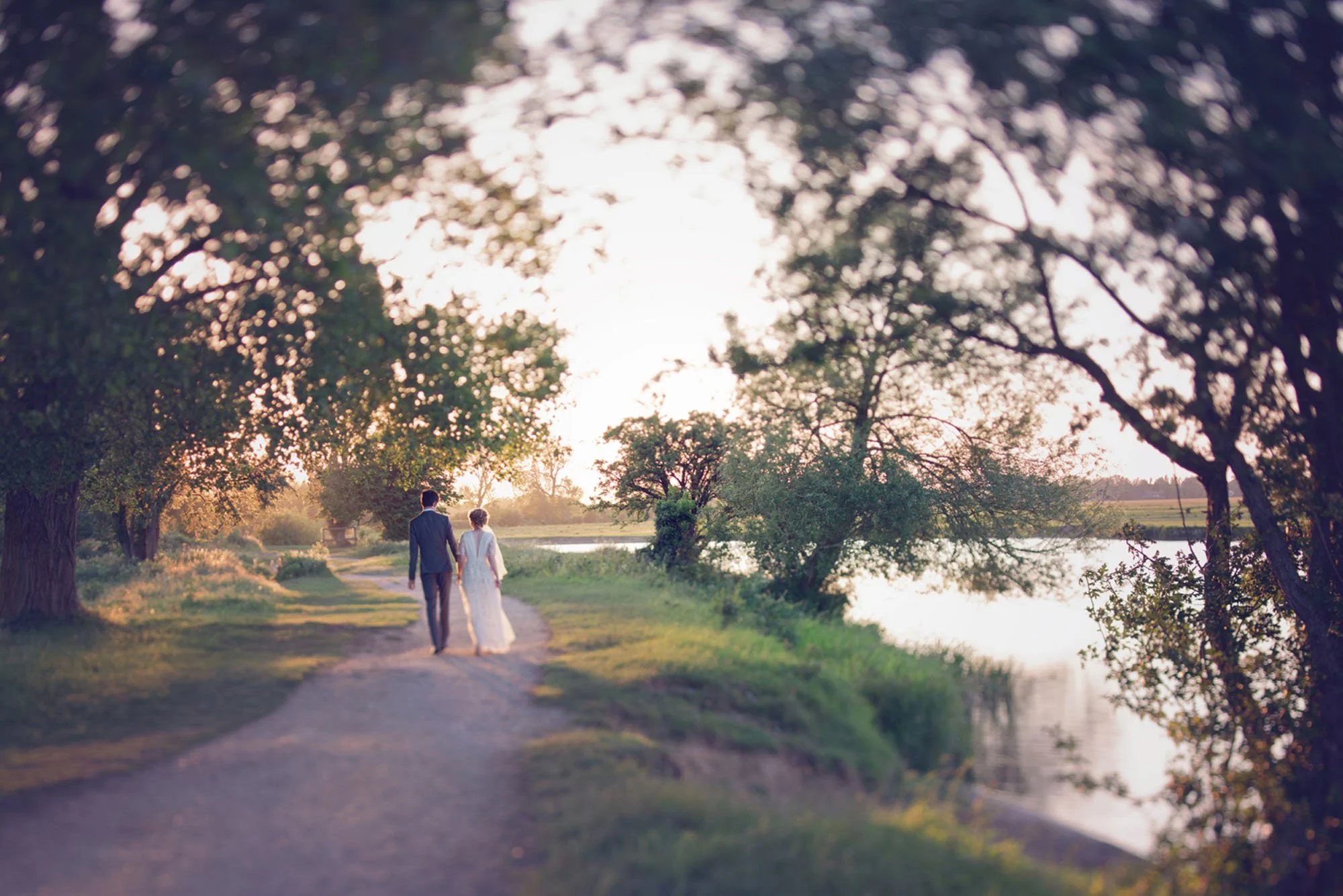 Bride and groom walk hand in hand by the river Cherwell during sunset at their weekday wedding at The Perch in Oxford.