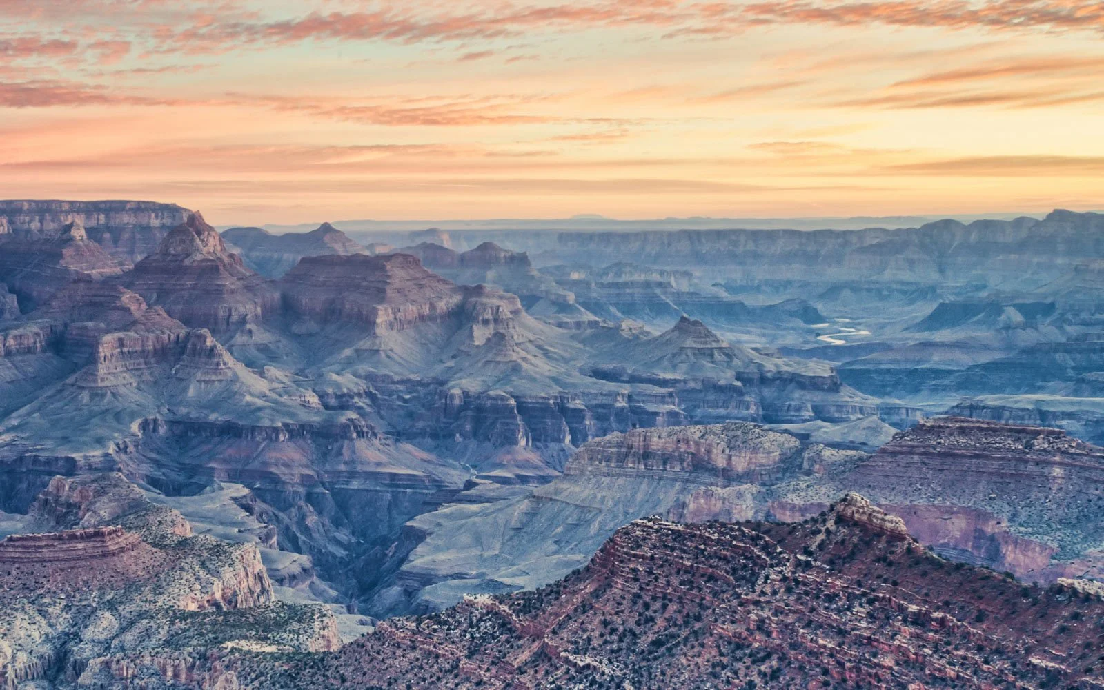 Sunset over the Grand Canyon with layered rock formations and a sky with pink and orange clouds.