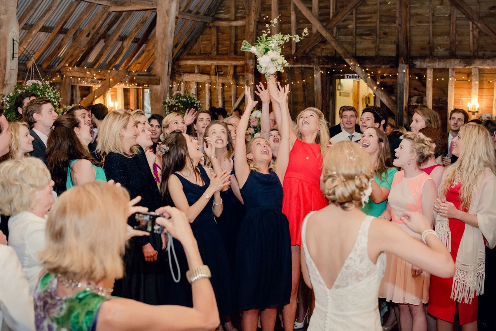 Eager arms reach up to catch the bride's bouquet during a barn wedding in Surrey