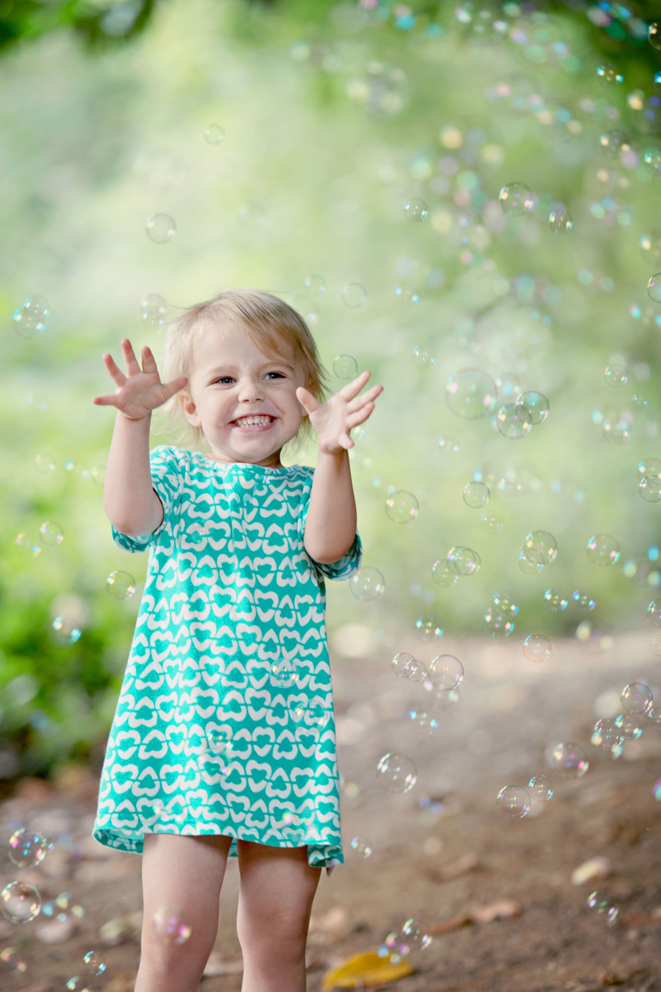 A little girl smiles and holds her hands up as she's surrounded by bubbles in Cannizaro Park in Wimbledon in south west London