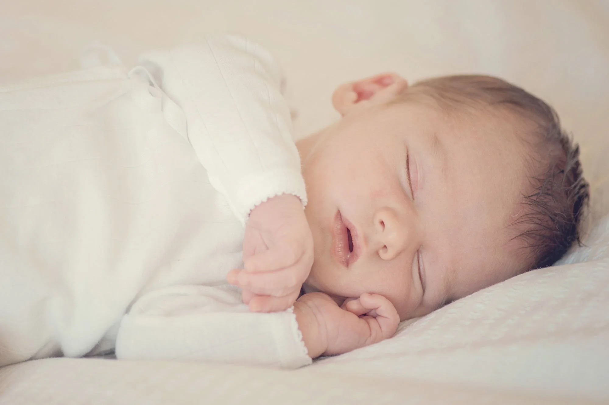 A newborn baby sleeps peacefully with one hand curled under her cheek, during a newborn shoot in Highgate in north London.