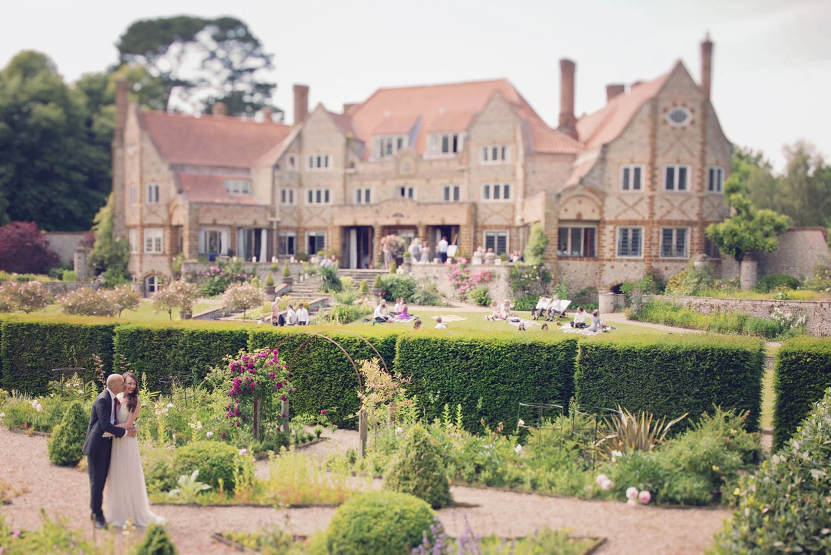 A groom kisses his bride with their venue Voewood in Norfolk in the background