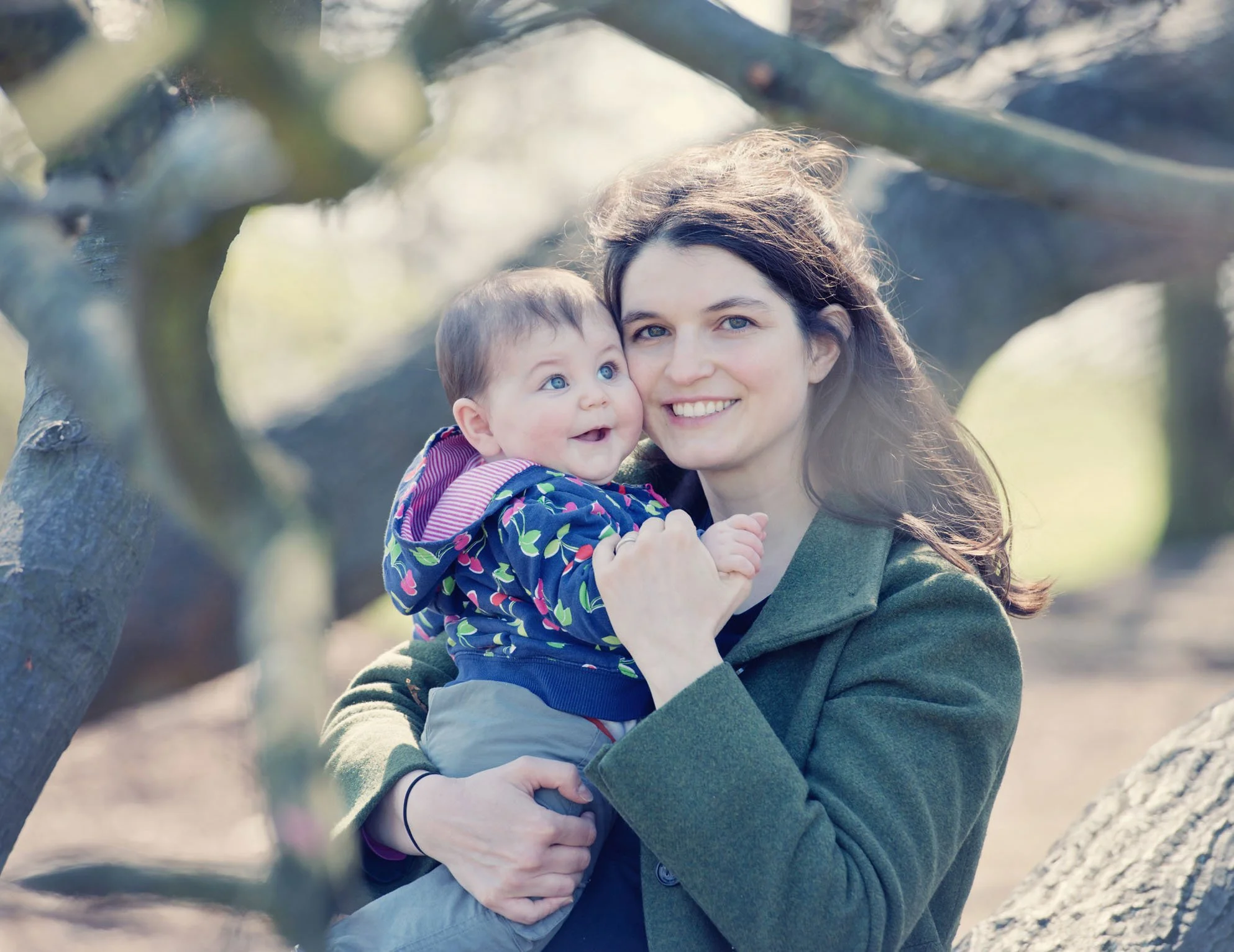 A mother smiles proudly at the camera as she holds her six month old baby girl to her chest during a family photoshoot in Hampstead Heath