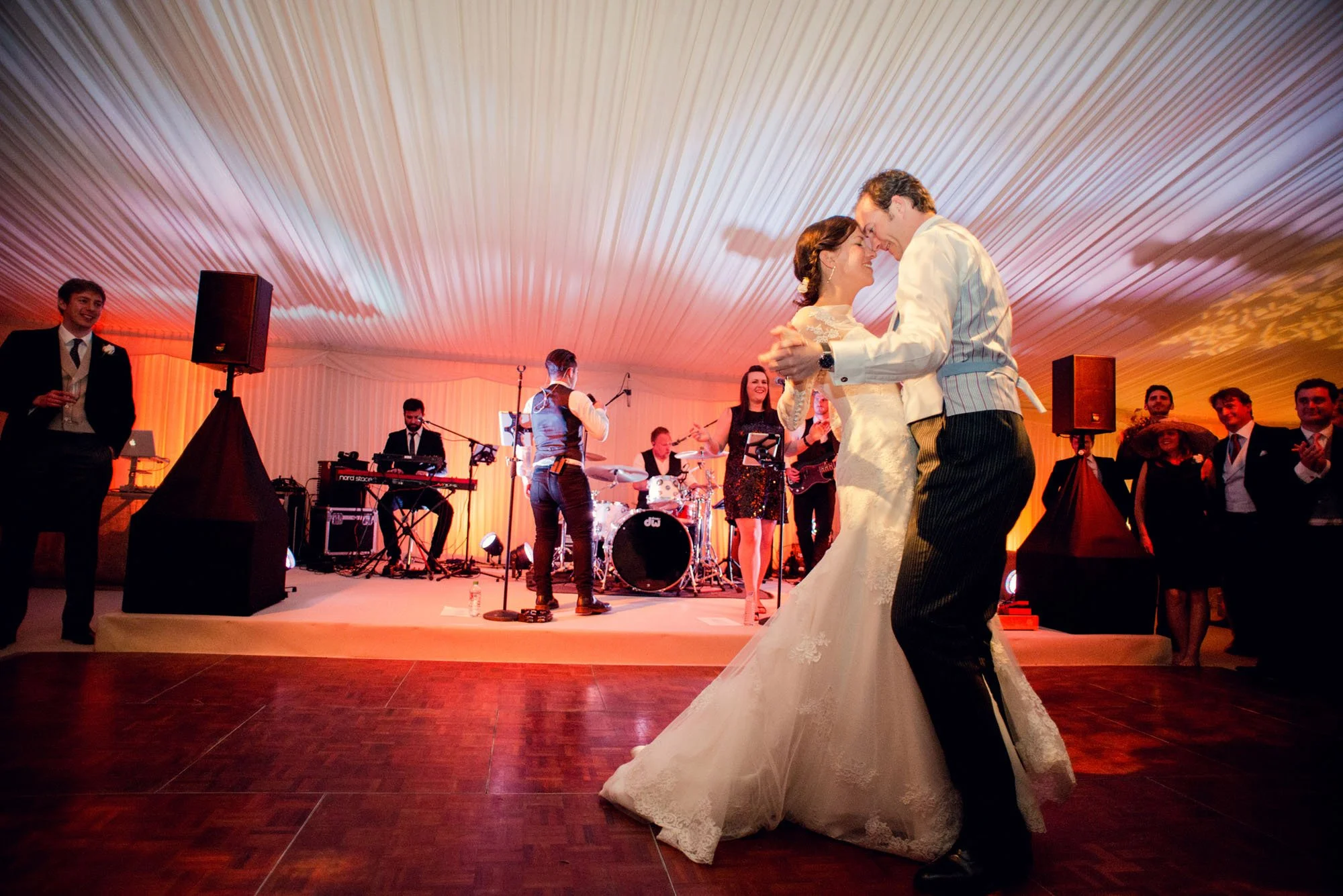 A bride and groom enjoy their first dance in front of a singer and band in a marquee in the garden of the bride's family home in Kent